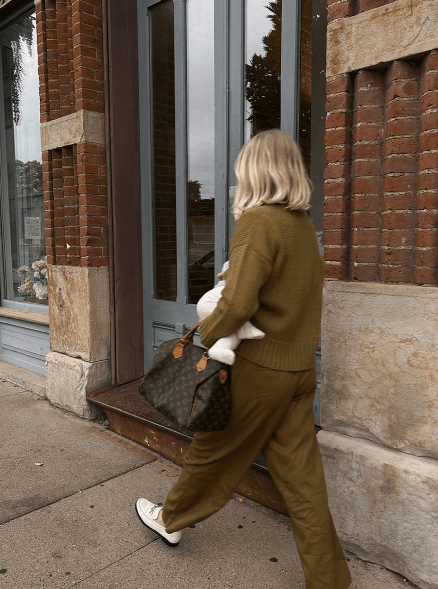 A woman walking down the street with an Alfred Trouser - Olive purse.
