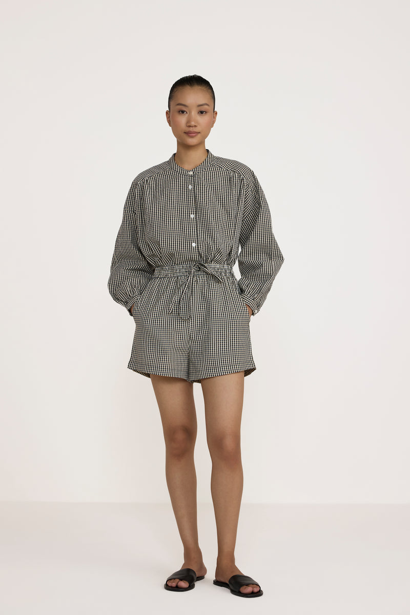 Person wearing a gray checkered shirt and shorts on a white background