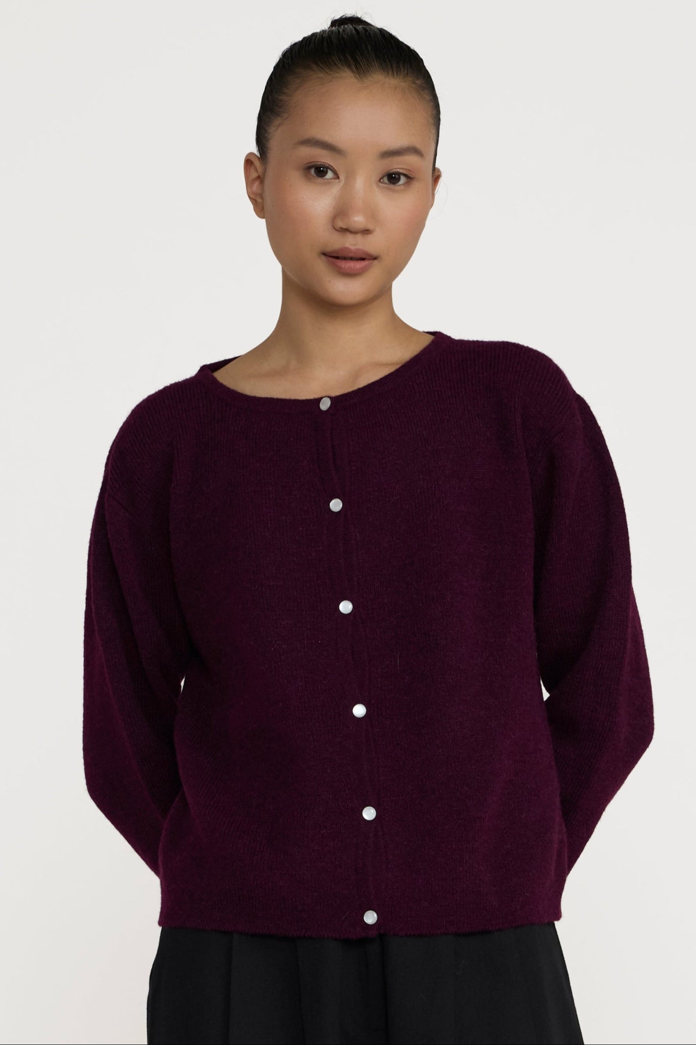 Person wearing a dark purple cardigan and black pants on a white background