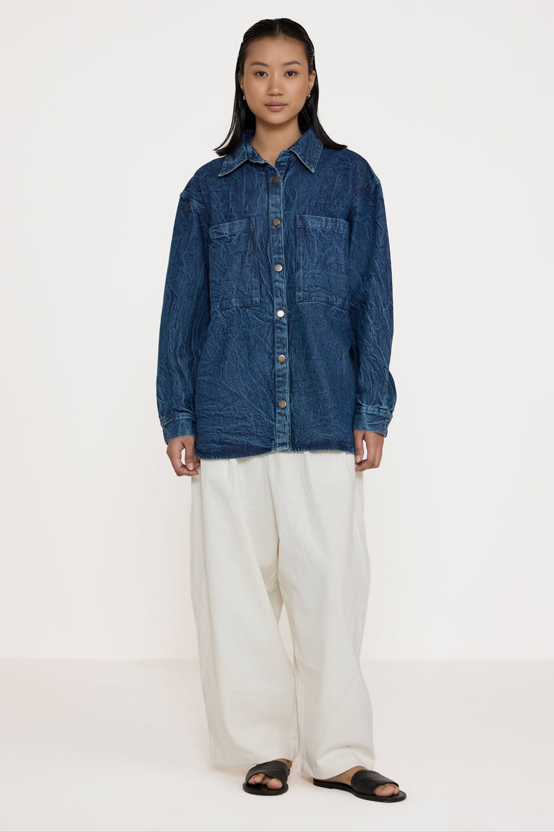 Person wearing a blue denim shirt and white pants on a white background