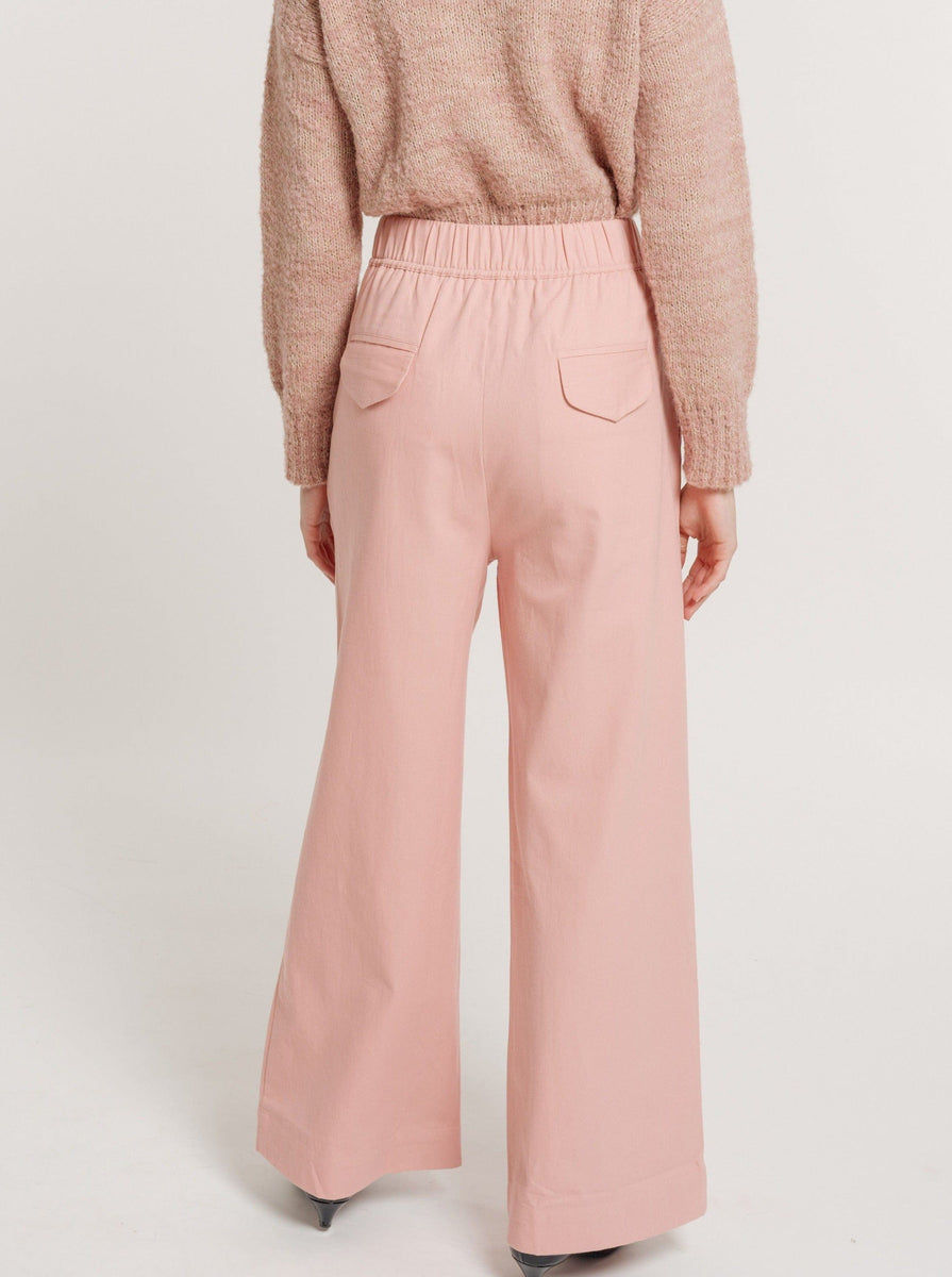 The back view of a woman wearing Hepburn Trouser - Pincushion Pink made with organic cotton and a beige sweater.