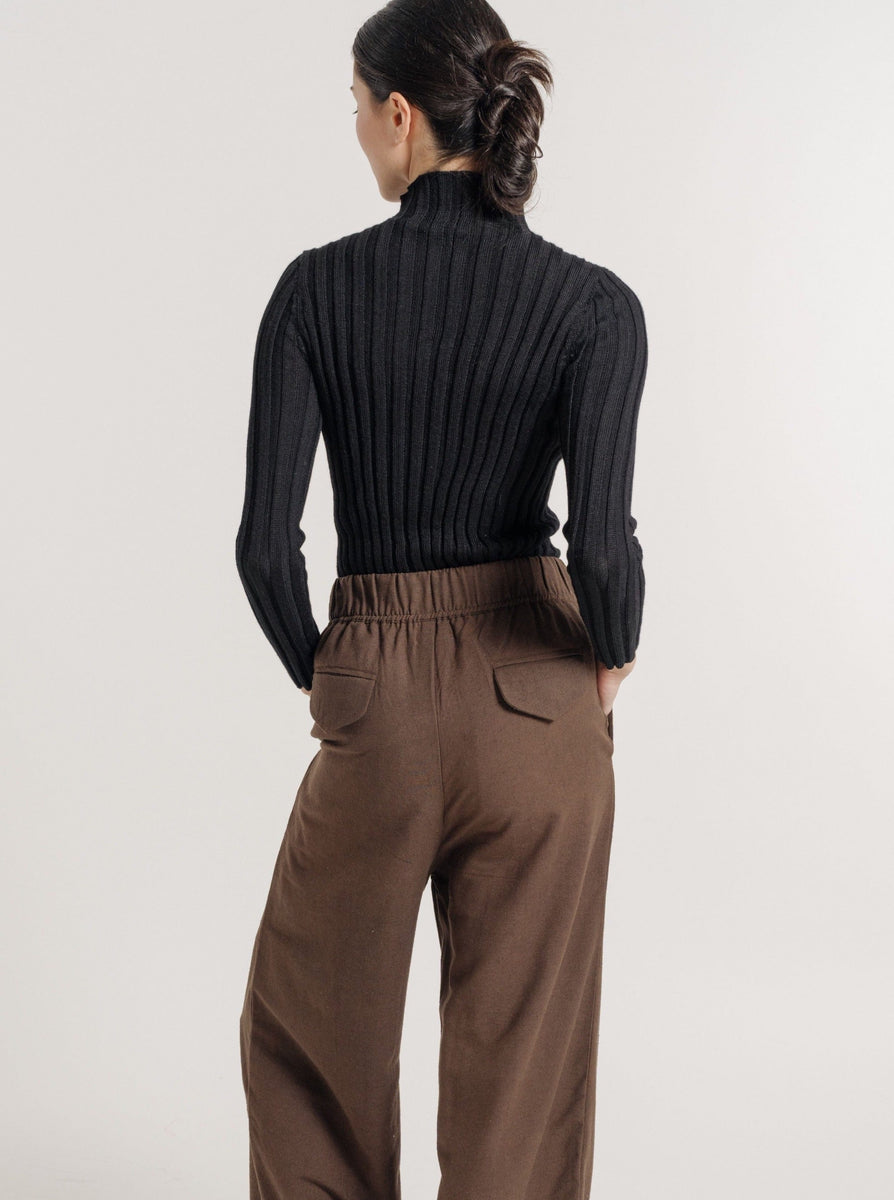 The back view of a woman wearing vintage-inspired brown wide leg pants and the Soa Ribbed Turtleneck - Black.