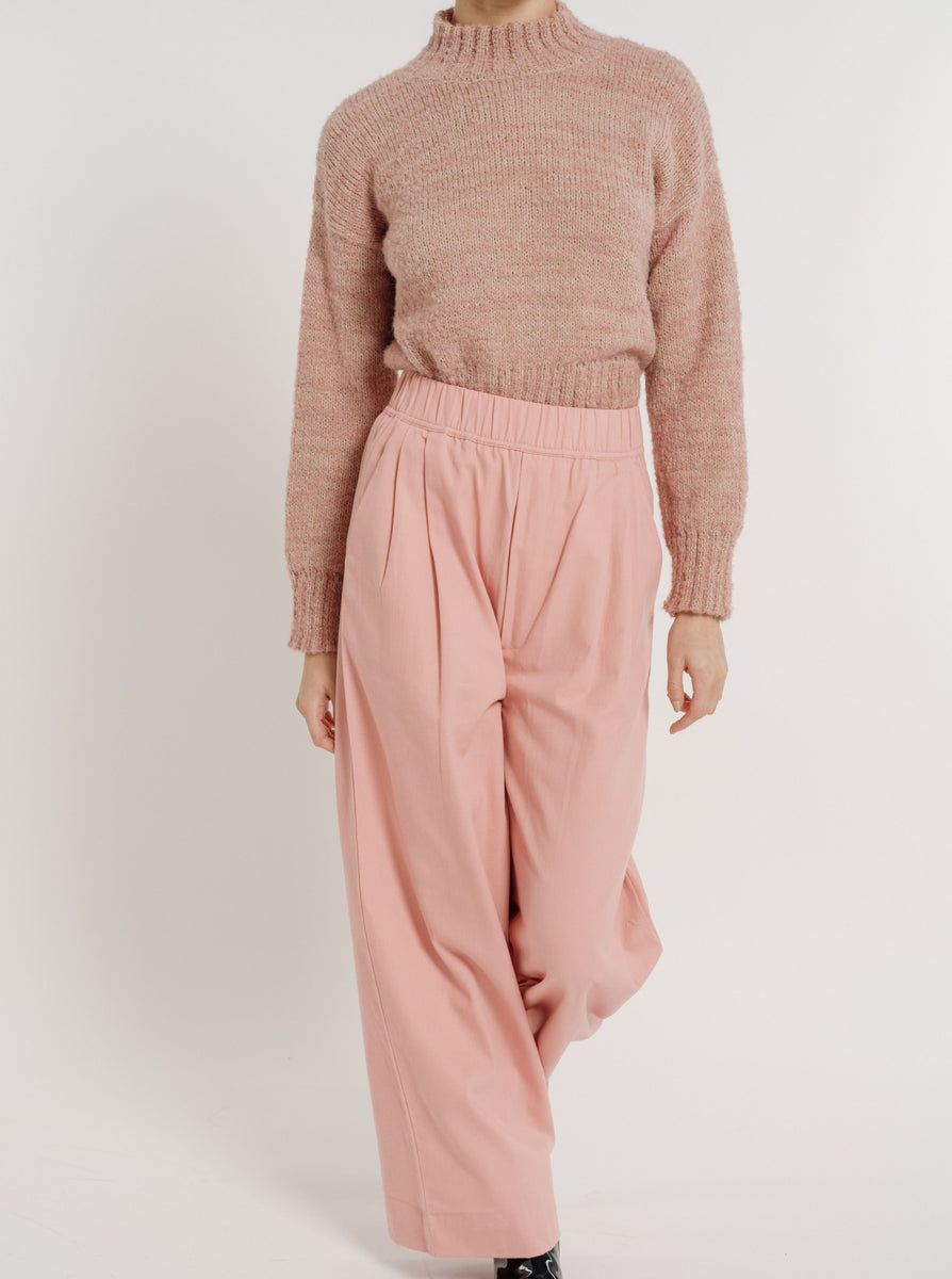 The model is wearing an organic cotton Hepburn Trouser - Pincushion Pink in a pink sweater.