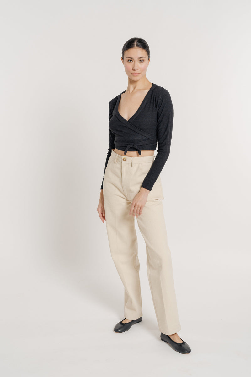 Woman standing in a studio wearing a Ballet Wrap Top - Black Silk Noil, beige trousers, and black flats handmade in India.