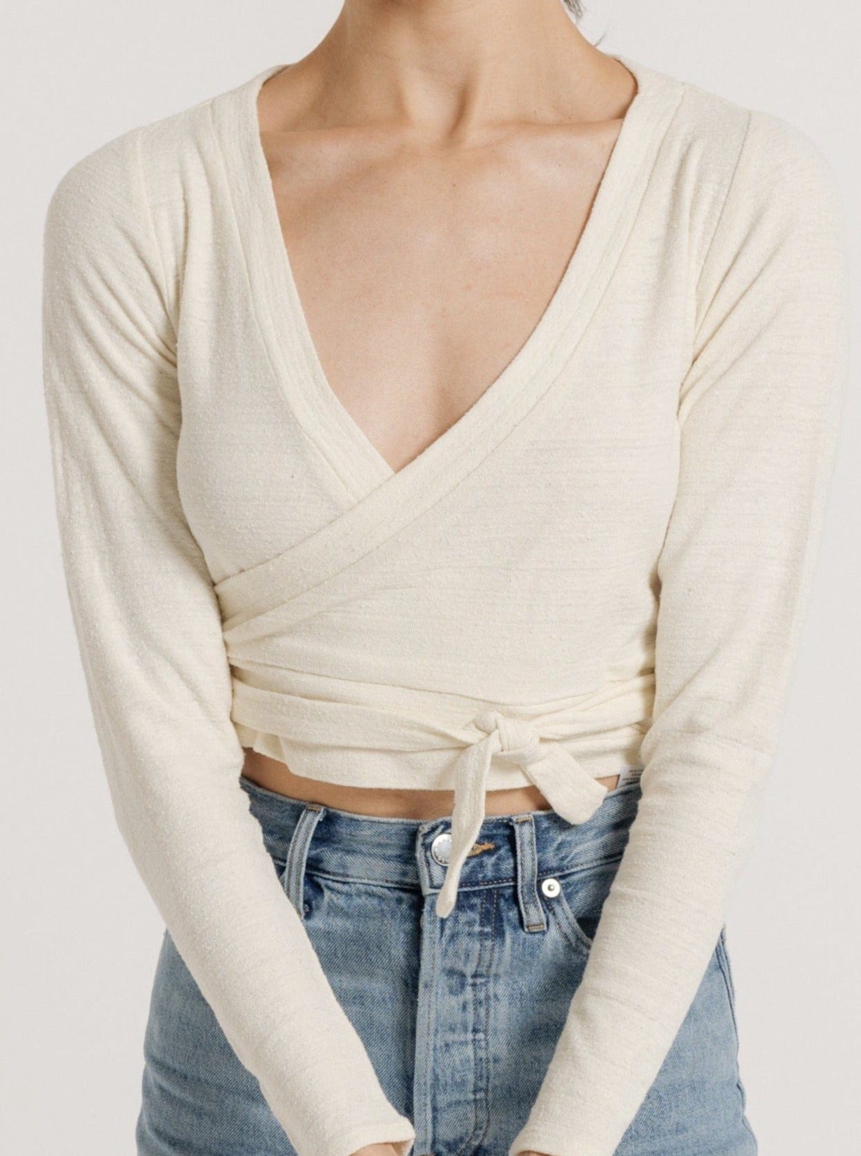 A woman in a Ballet Wrap Top - Ivory Silk Noil and blue jeans standing against a neutral background.