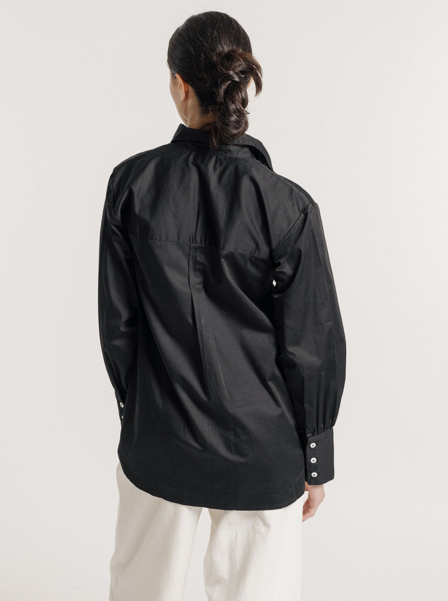 The back view of a woman wearing a black Museo Button Up - Black shirt and white pants.