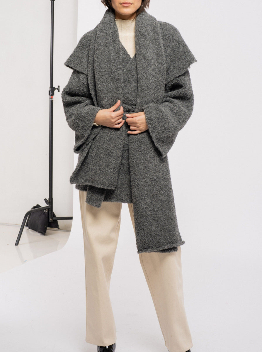 The model is wearing a Heirloom Knit Scarf - Charcoal Grey and beige pants.
