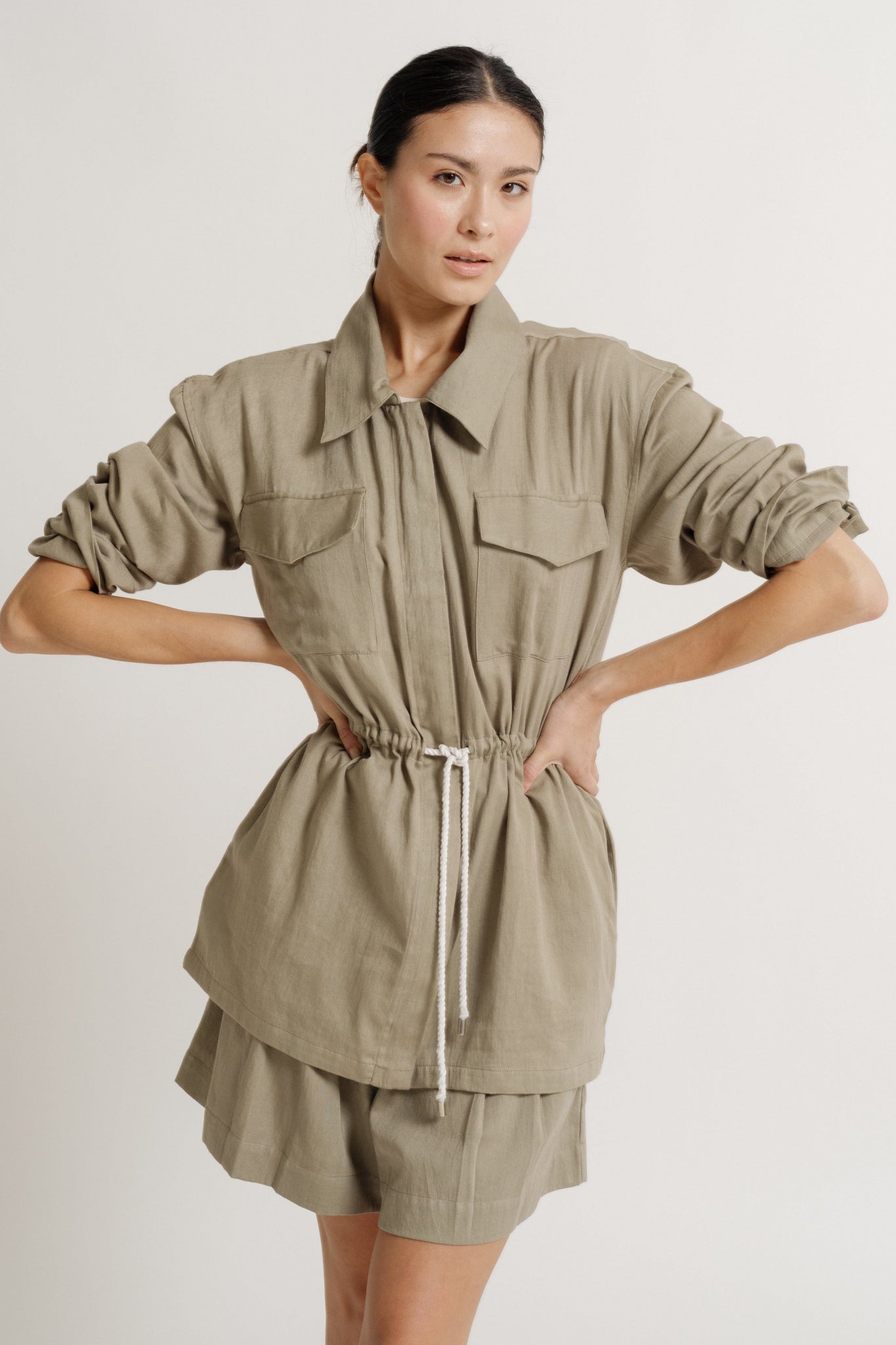 The model is wearing a Drawstring Utility Jacket - Putty and shorts made of lightweight cotton sateen fabric.