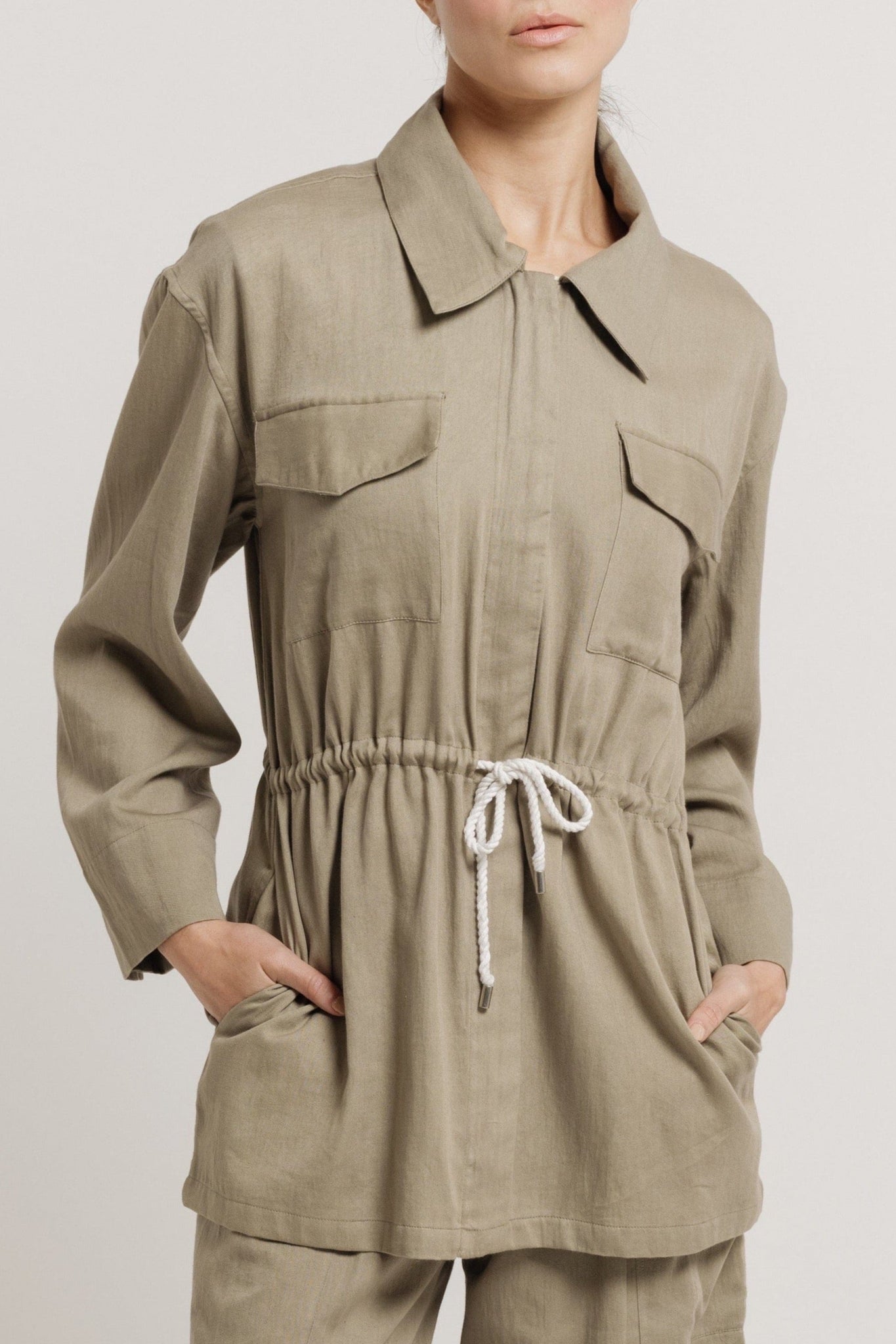 The model is wearing a lightweight Drawstring Utility Jacket - Putty and pants.