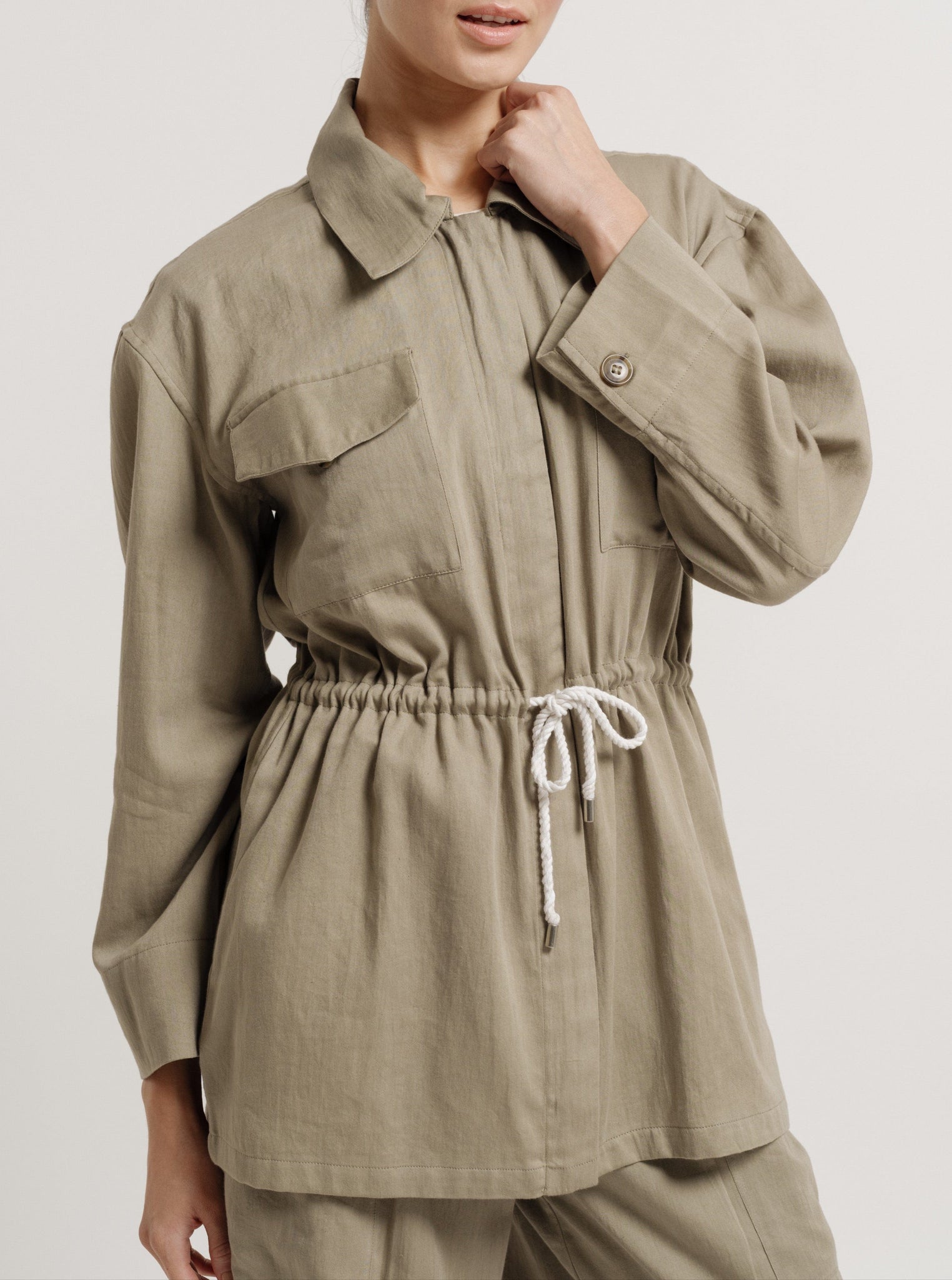 The model is wearing a lightweight Drawstring Utility Jacket - Putty made of cotton sateen.