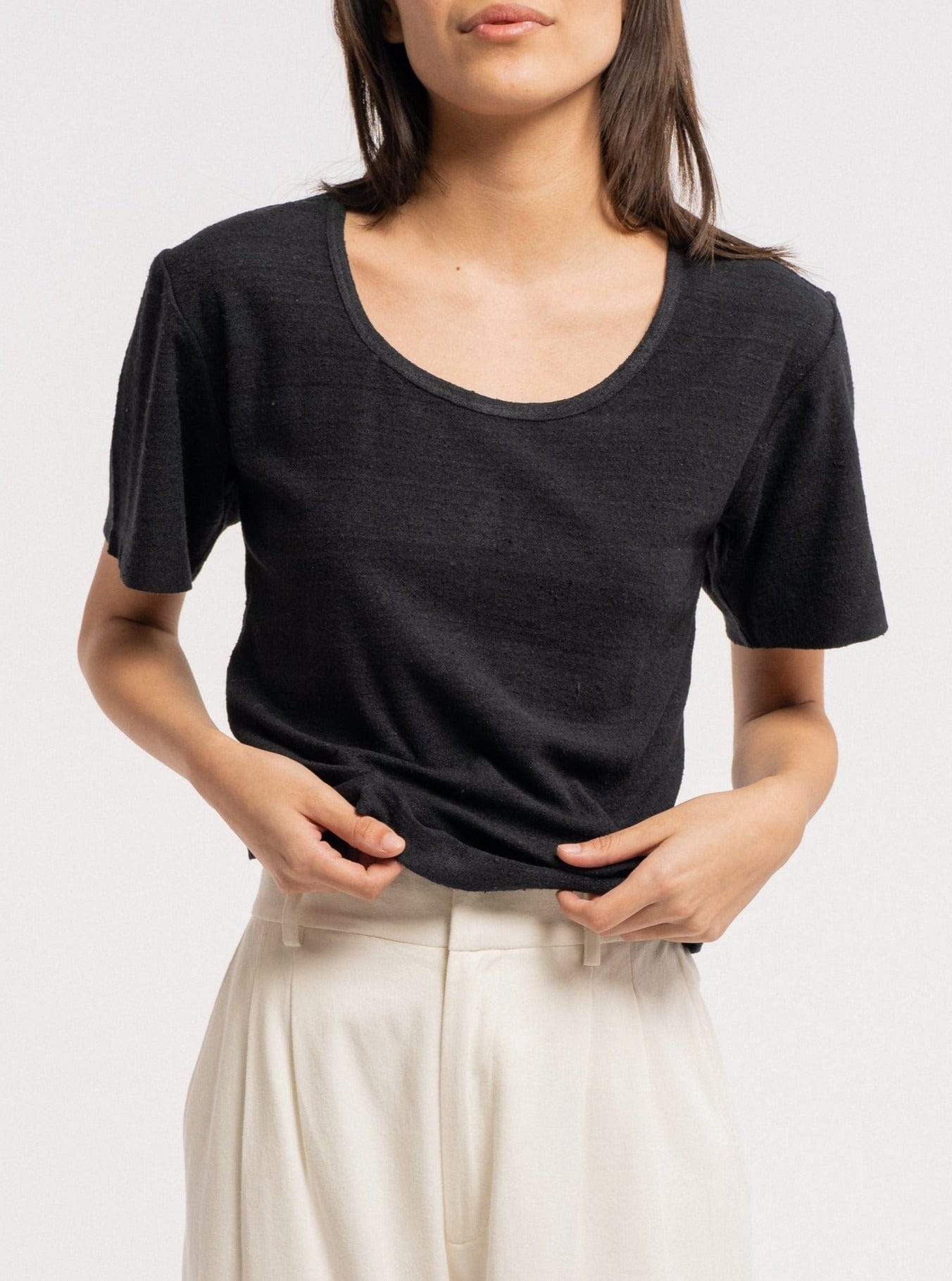 A woman wearing a Baby Tee - Black - pre-order and white pants.