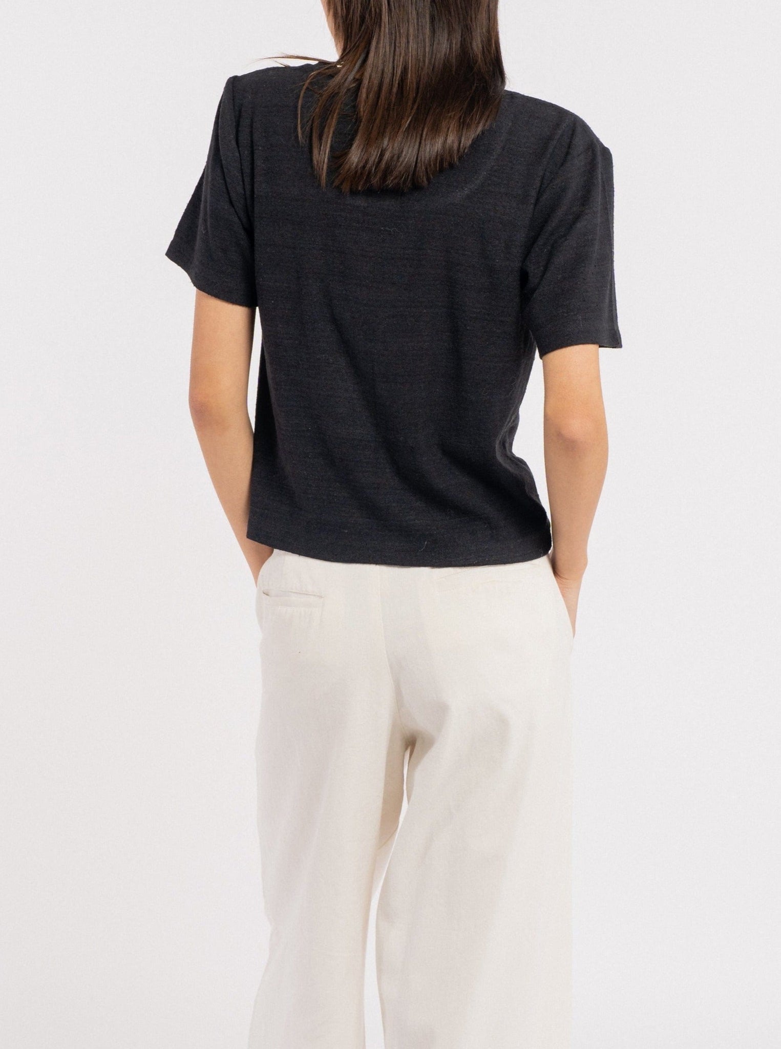 The back view of a woman wearing a Baby Tee - Black - pre-order and wide leg pants.