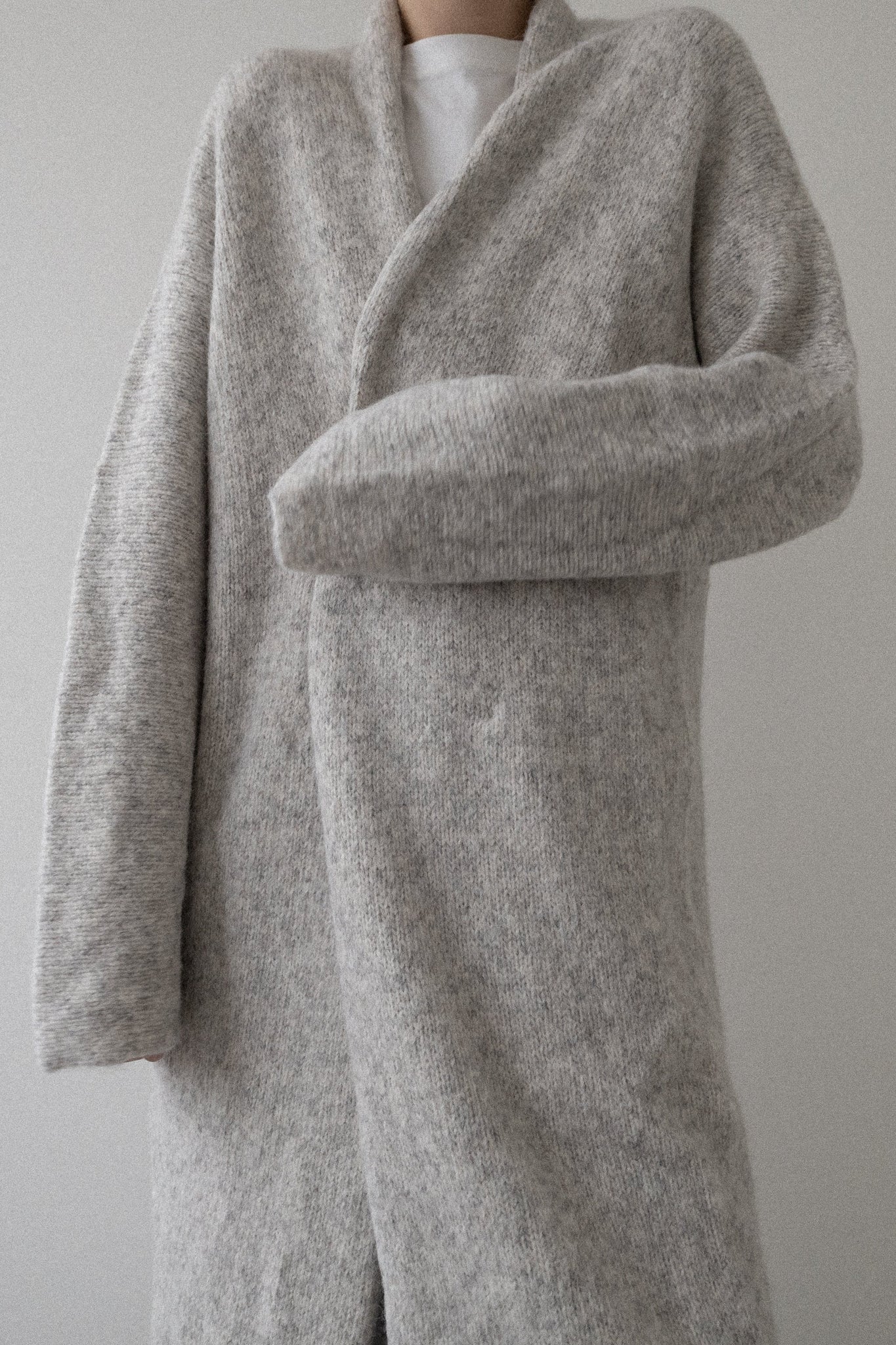 Person wearing a long gray coat against a plain background