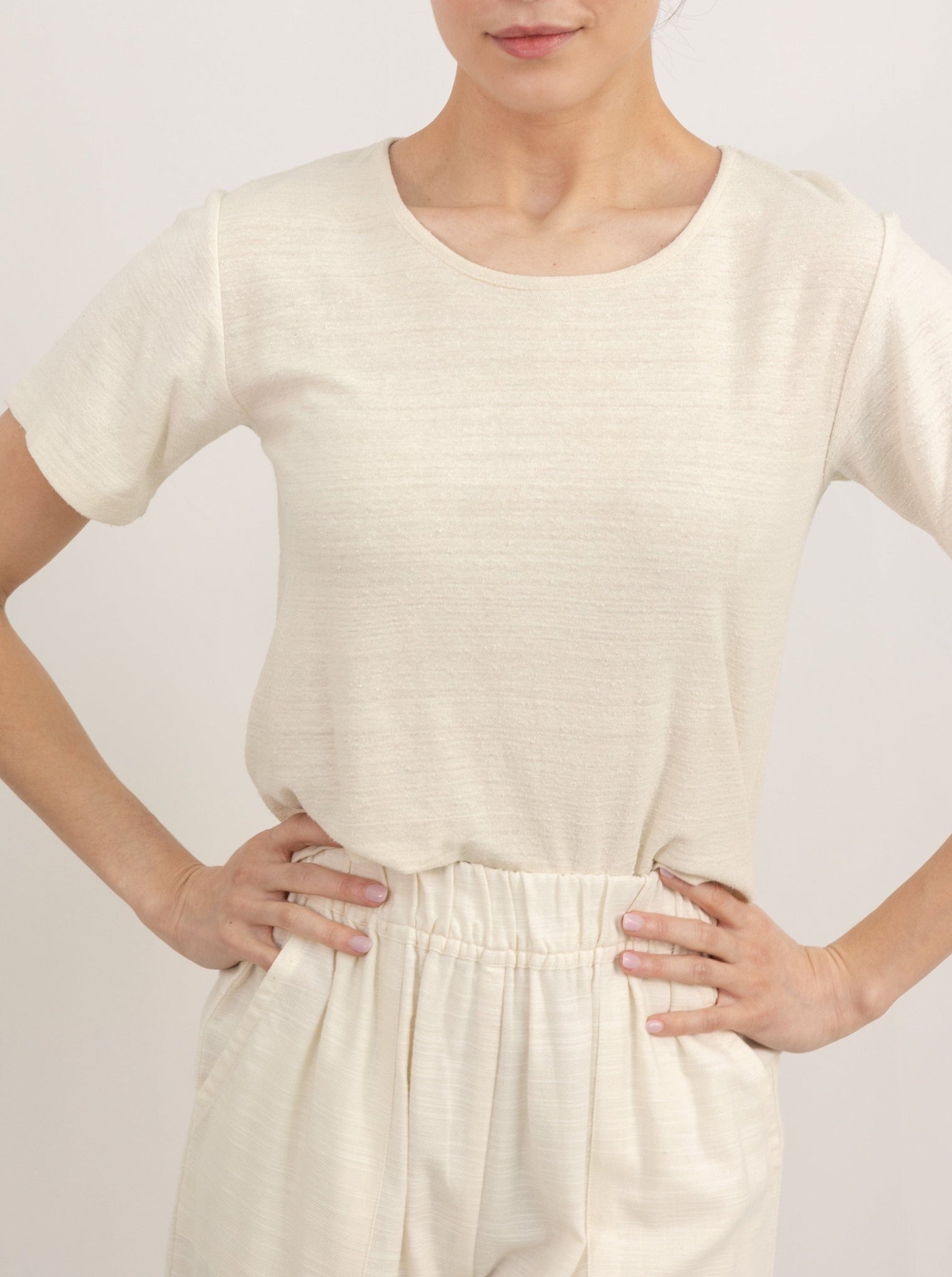 A woman with her hands on her hips, wearing a Cropped Crew T-Shirt - Ivory Silk Noil.