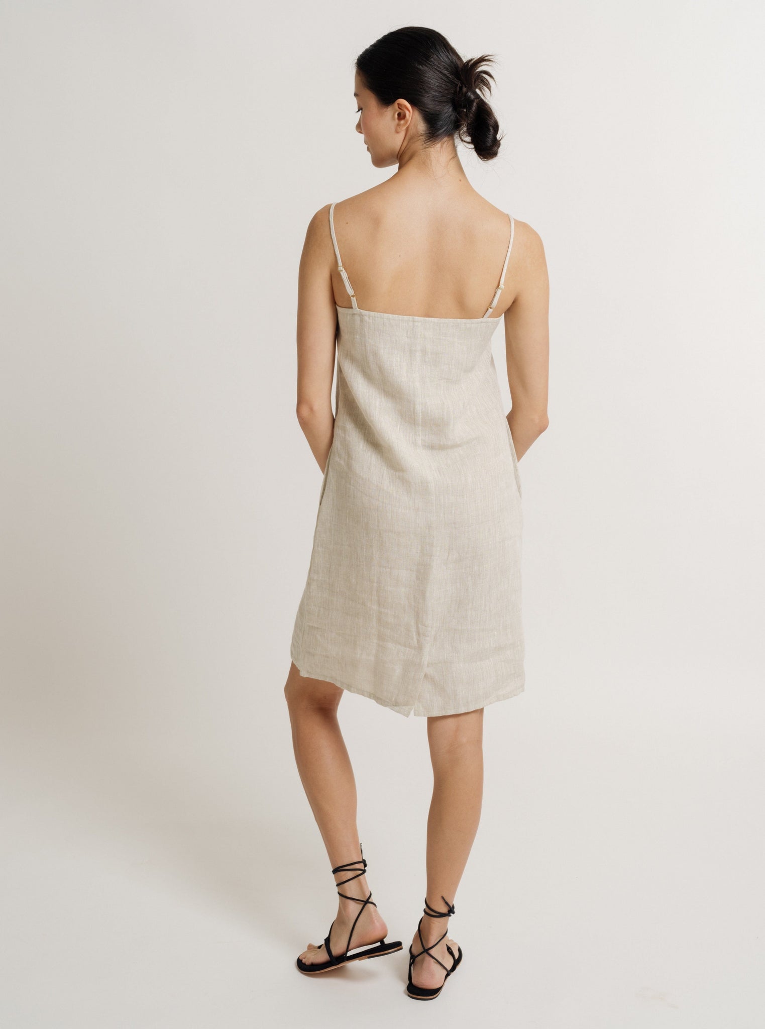 The back view of a woman wearing a Linen Mini Dress - Natural Linen - Pre-order with adjustable straps.