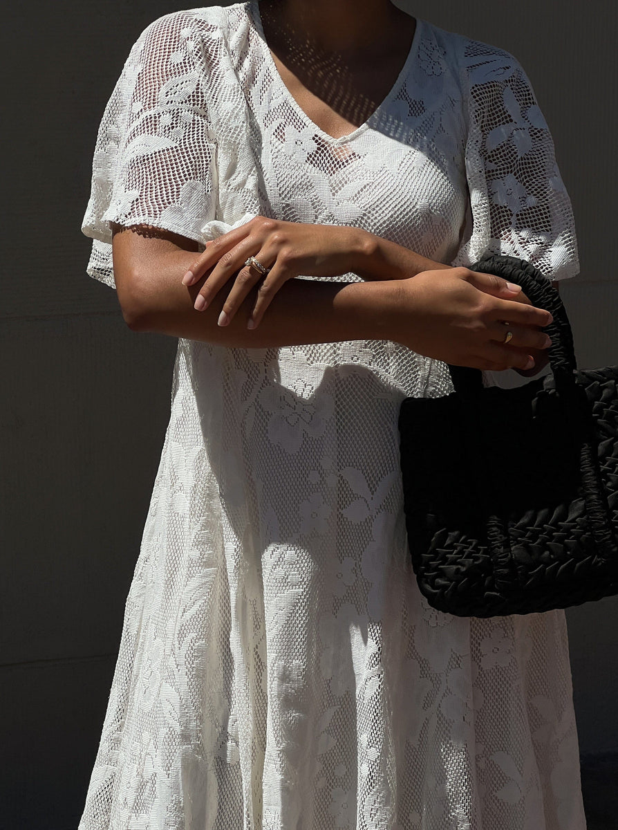 A woman in the Ailes Dress - Ivory - Sample holding a black purse in like-new condition.