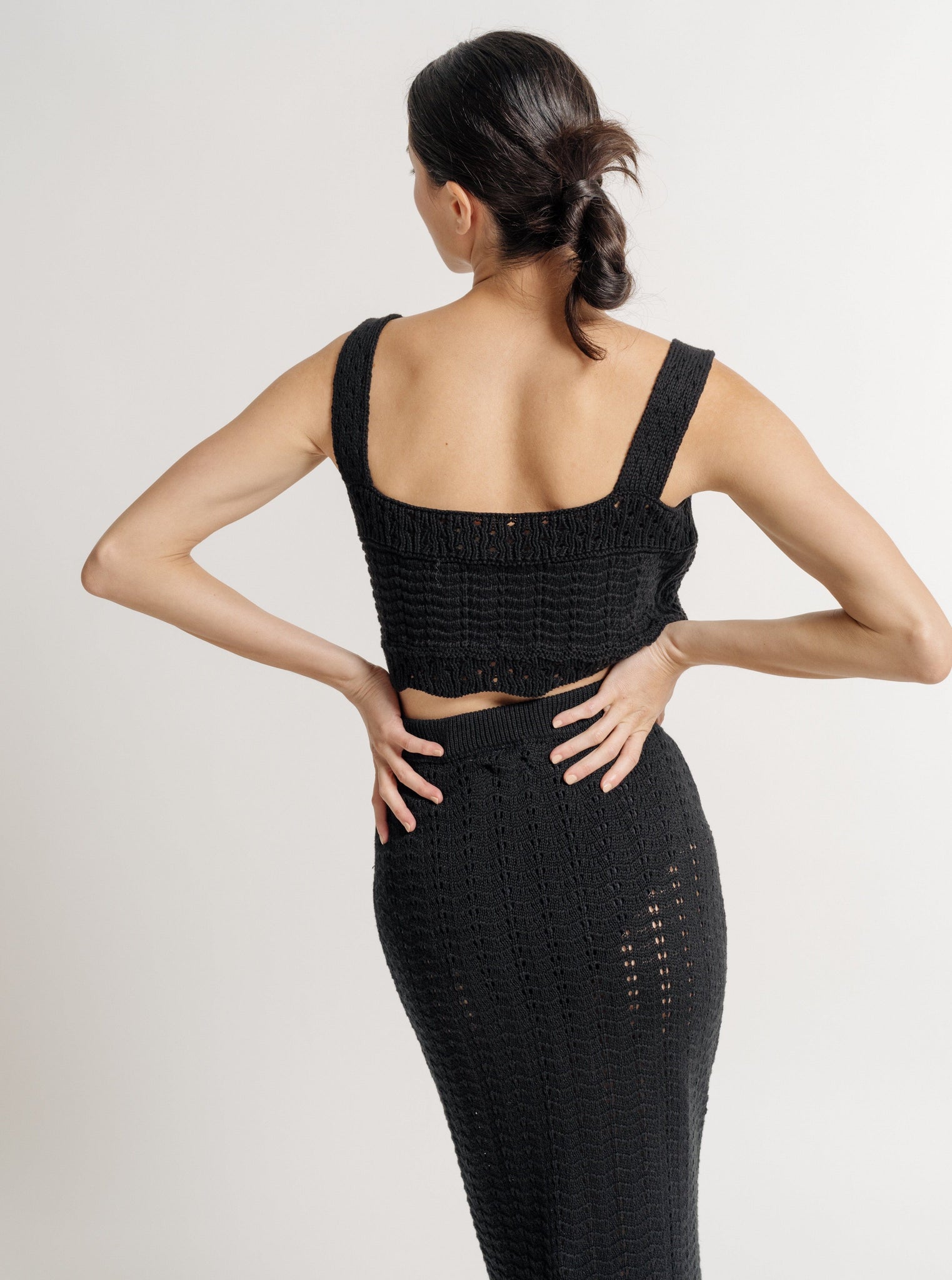 The back view of a woman wearing the Lyric Crochet Crop Tank - Black - Pre-order.