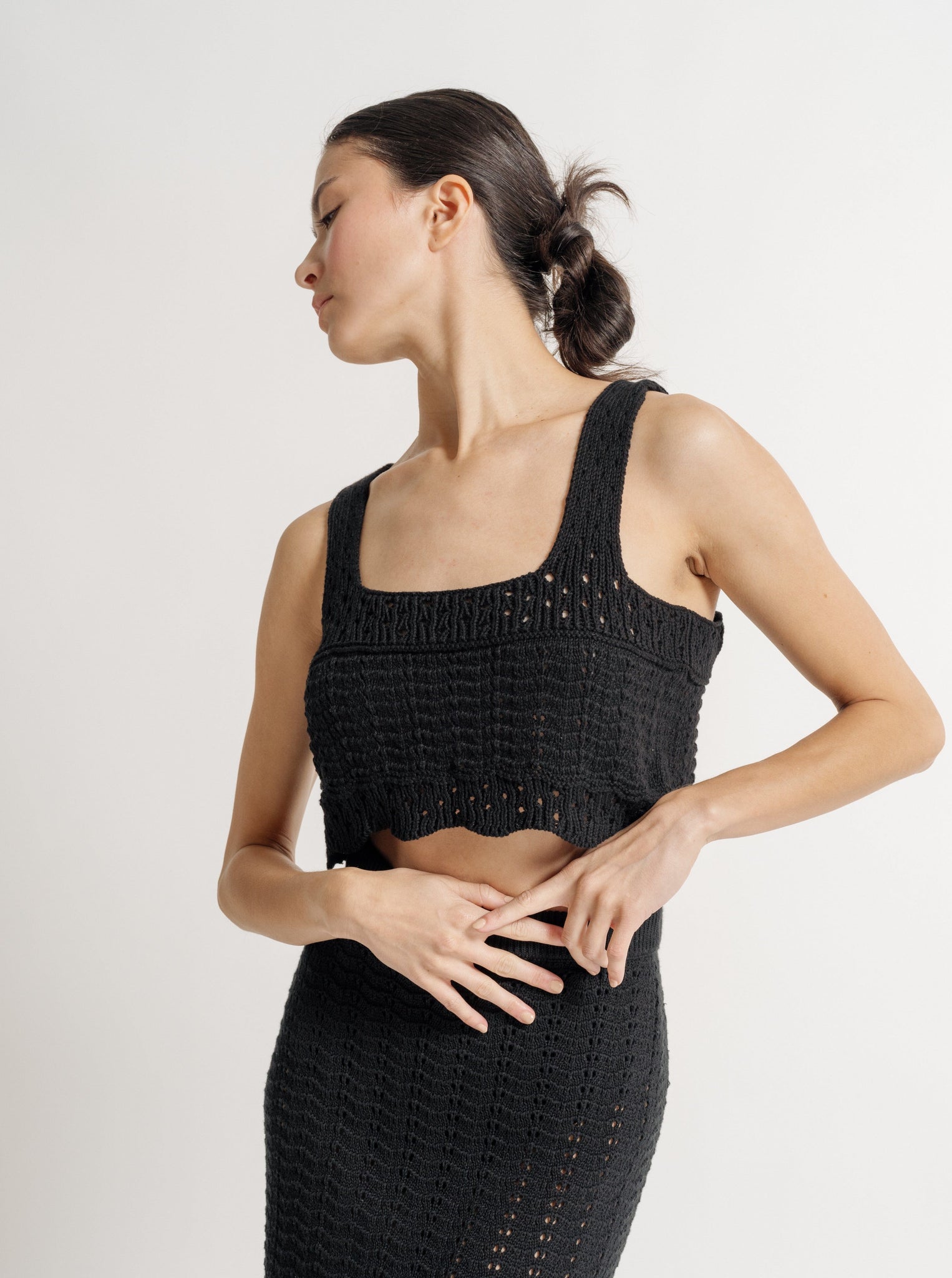 A woman posing in a Lyric Crochet Crop Tank - Black with her hands on her waist, looking to the side against a neutral background.