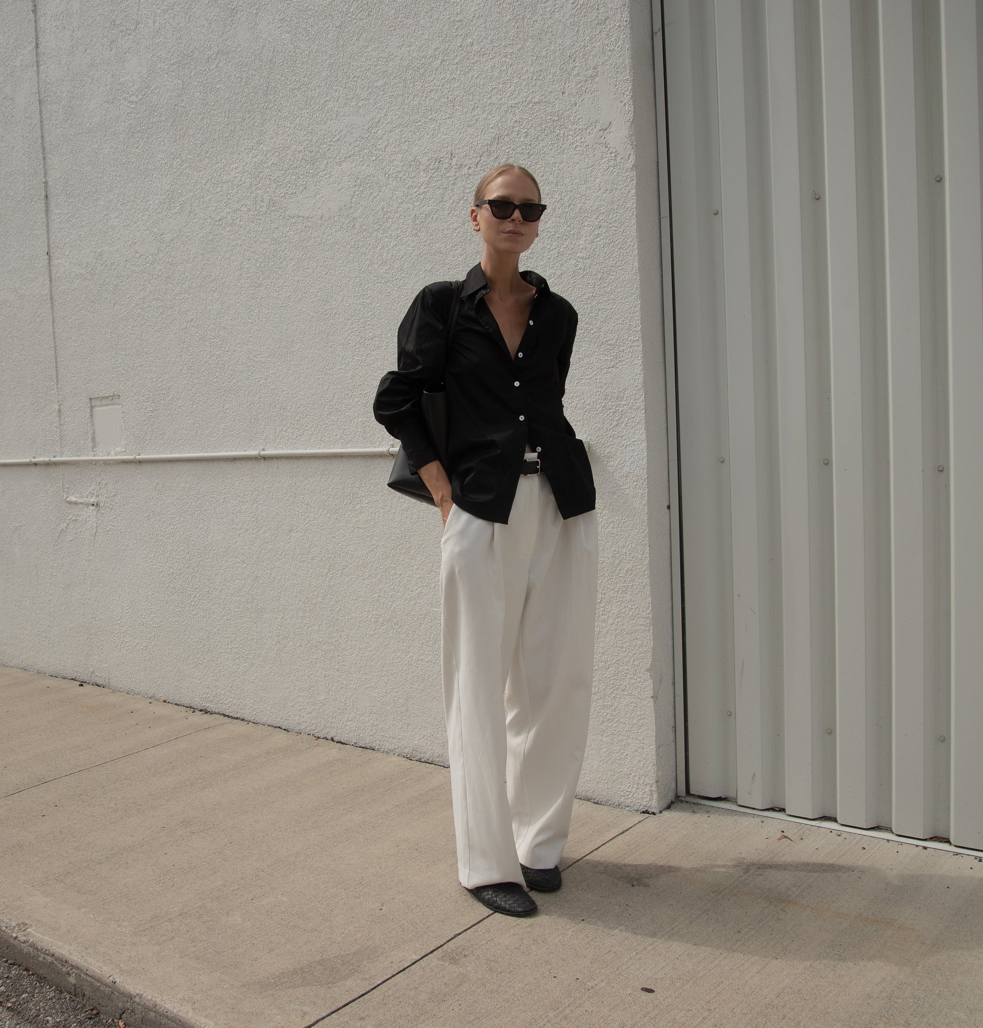 A woman wearing a Museo Button Up - Black made of organic cotton, paired with white pants.