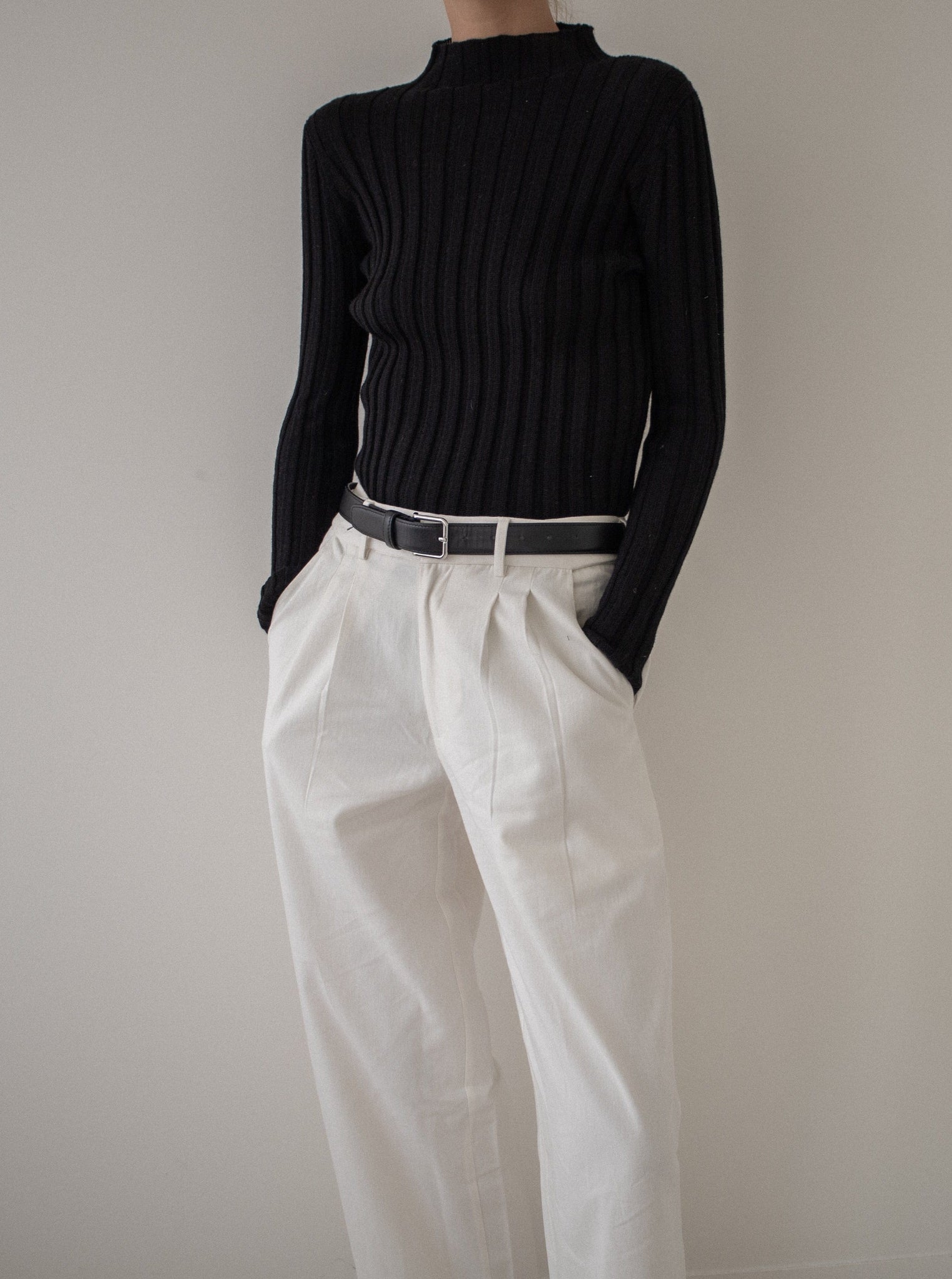A woman wearing a Soa Ribbed Turtleneck - Black sweater and ethically-sourced white pants.