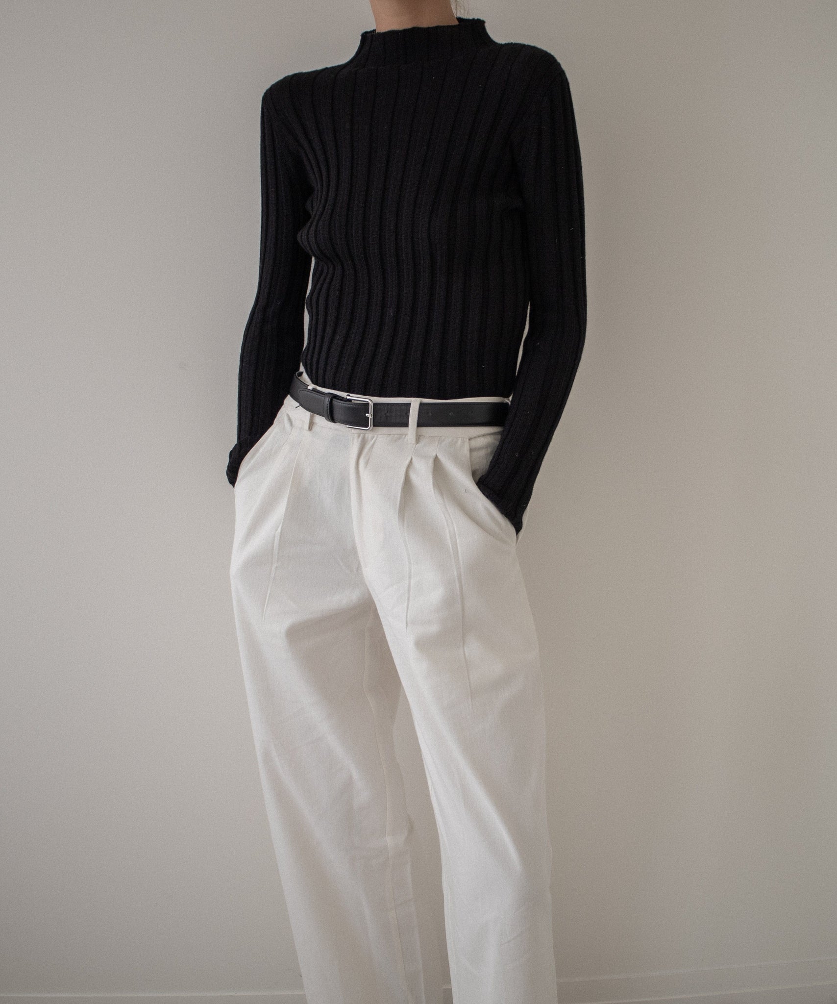 A woman wearing a black sweater and Alfred Trouser - Ivory pants.