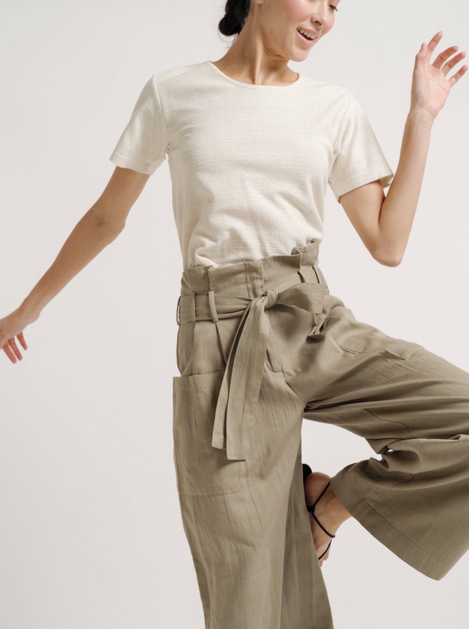 A woman wearing Paper Bag Pant - Putty - Pre-order in khaki cotton sateen fabric and a white t-shirt.