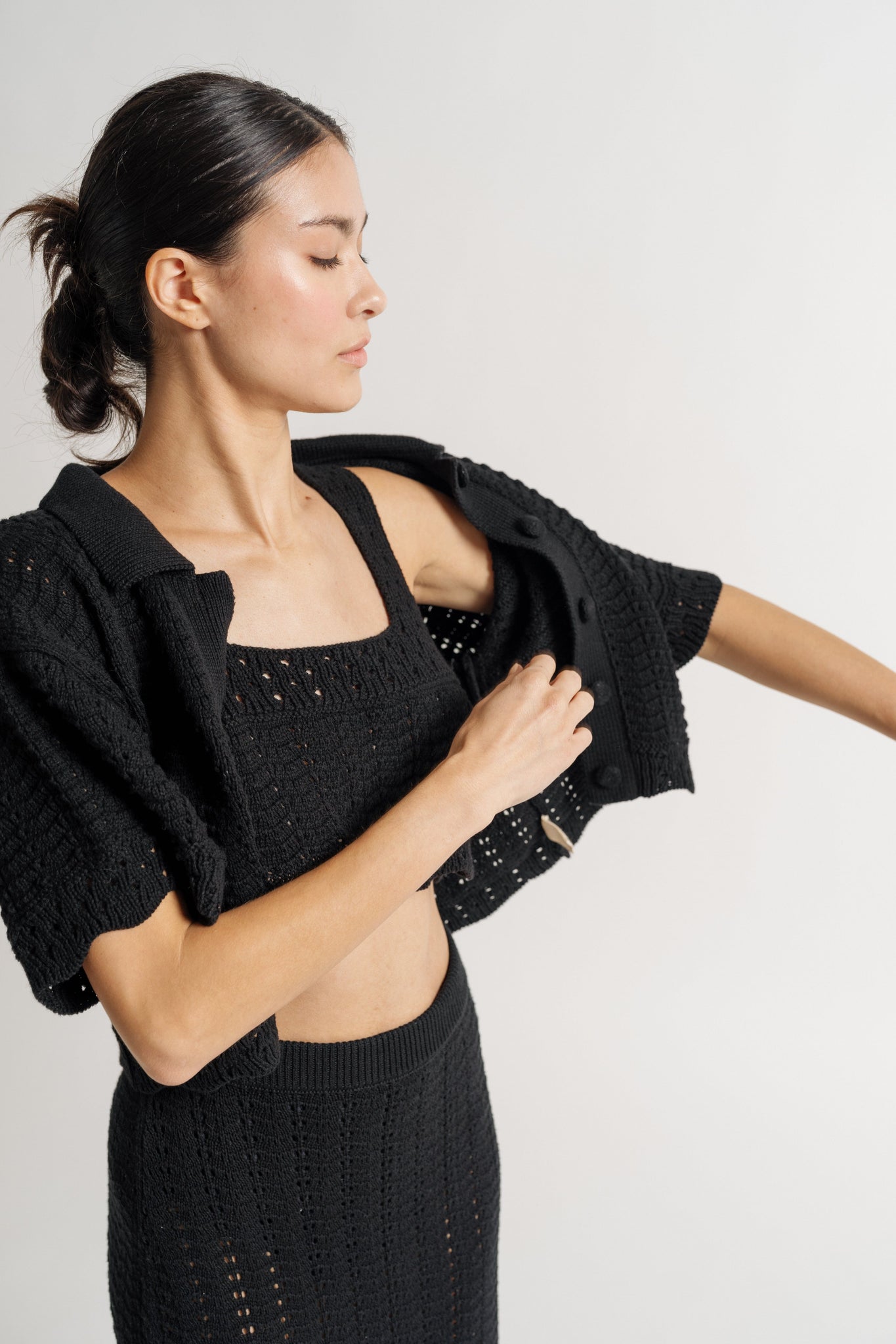 Woman in a Roma Crochet Top - Black putting on a cardigan.