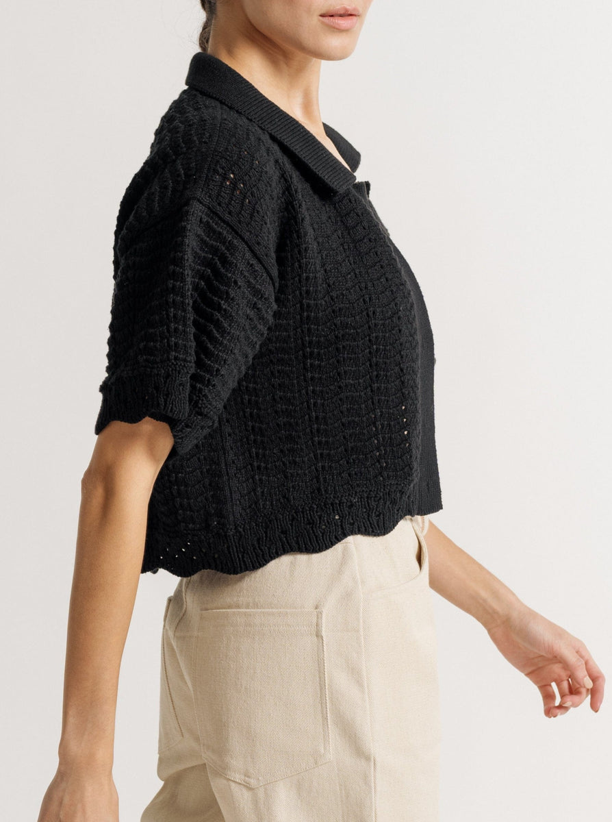 Sentence with product name: Woman in a Roma Crochet Top - Black and neutral-toned outfit walking against a white background.
