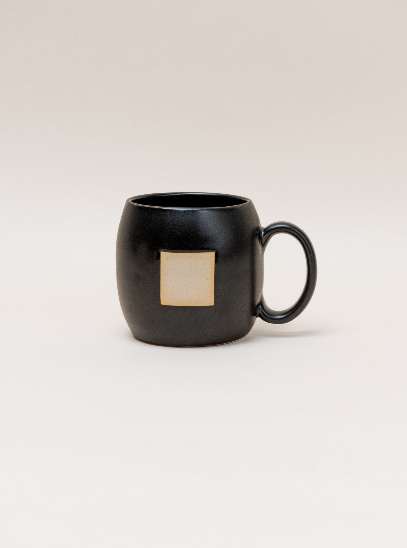 A Negative Space Mug - Black with a minimalist design featuring a gold square.