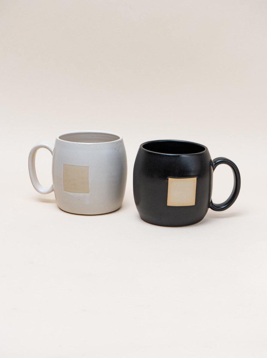 Two Negative Space black and white mugs on a minimalist white surface.