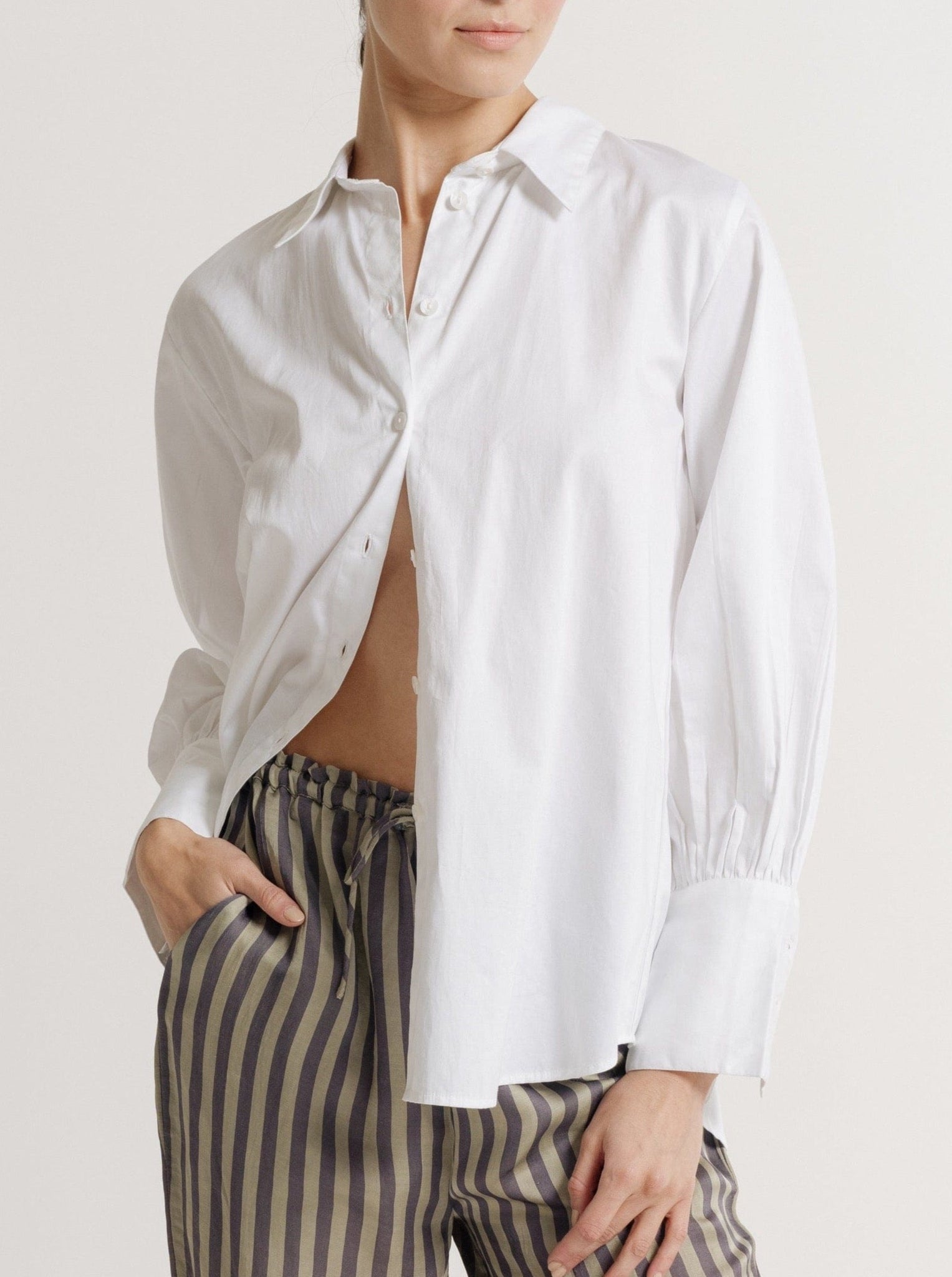 The model is wearing striped pants and a Museo Button Up - White Poplin shirt made from organic cotton.
