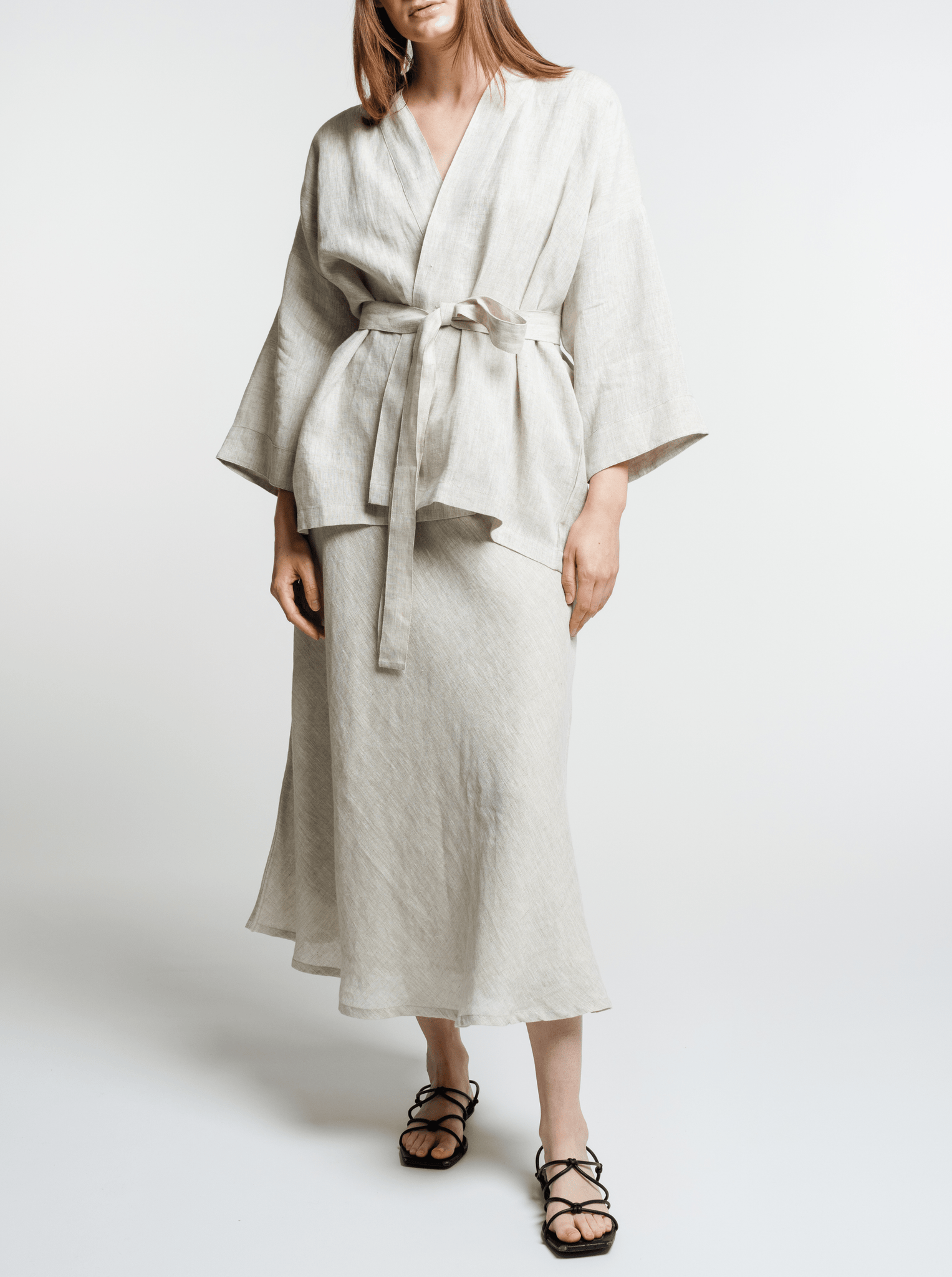 Woman modeling a light-colored organic Linen Wrap Top - Natural with a tie waist and flared sleeves, paired with black strappy sandals.
