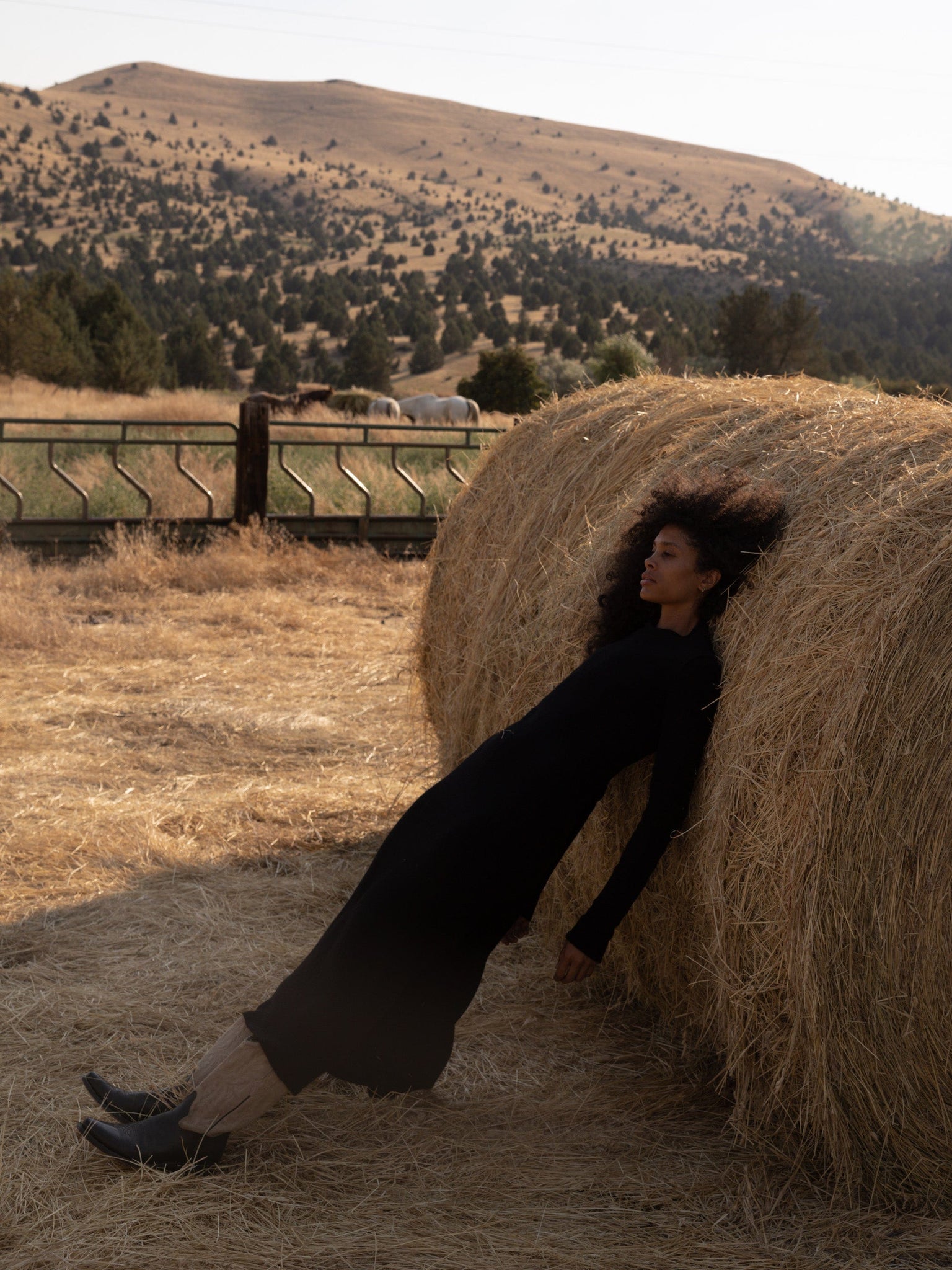 An ethically-sourced woman laying on a hay bale, showcasing the Ennis Dress - Black made from luxurious baby alpaca.