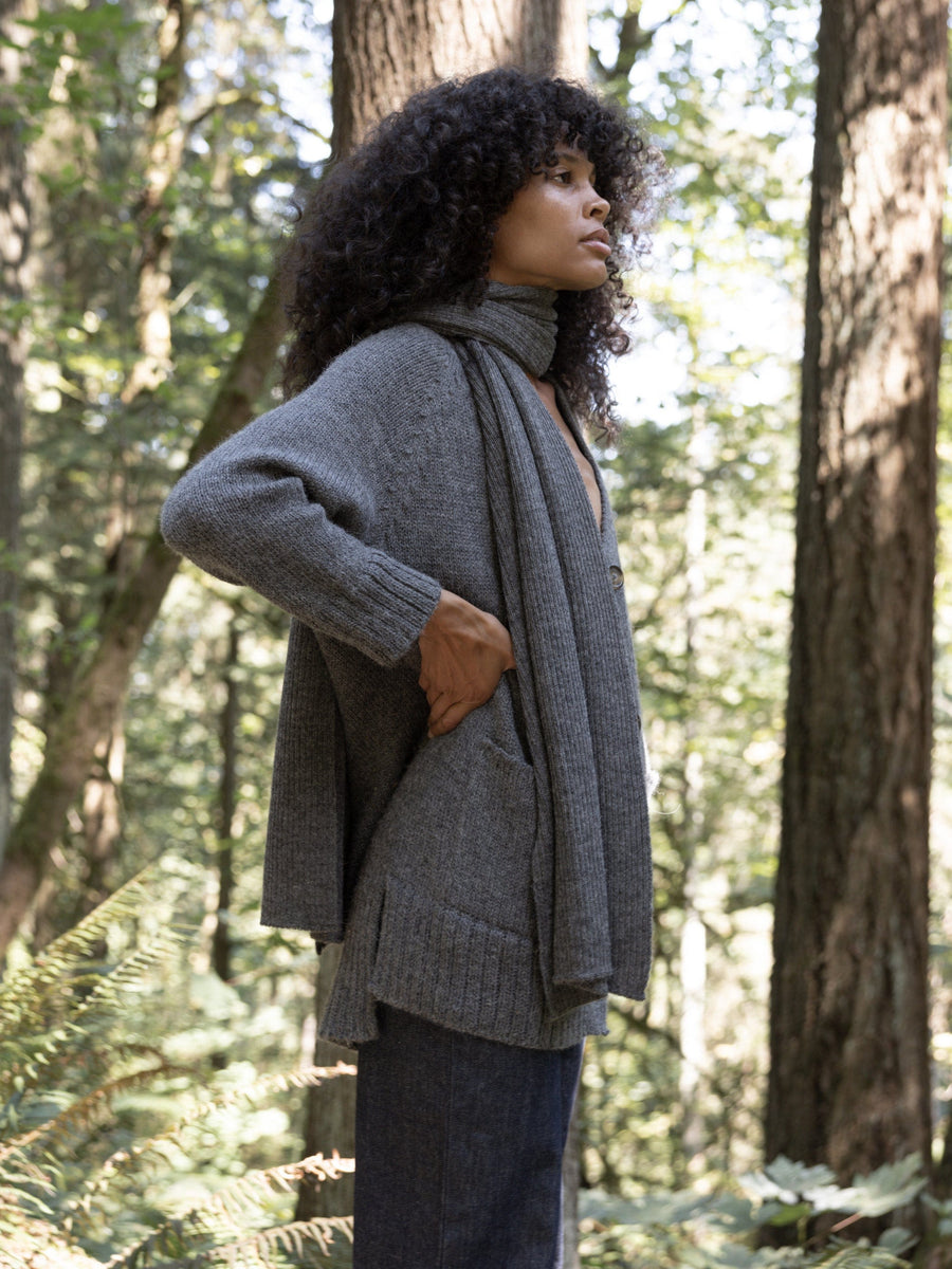 A woman in a gray Alpaca Ribbed Scarf - Smoke standing in the woods.