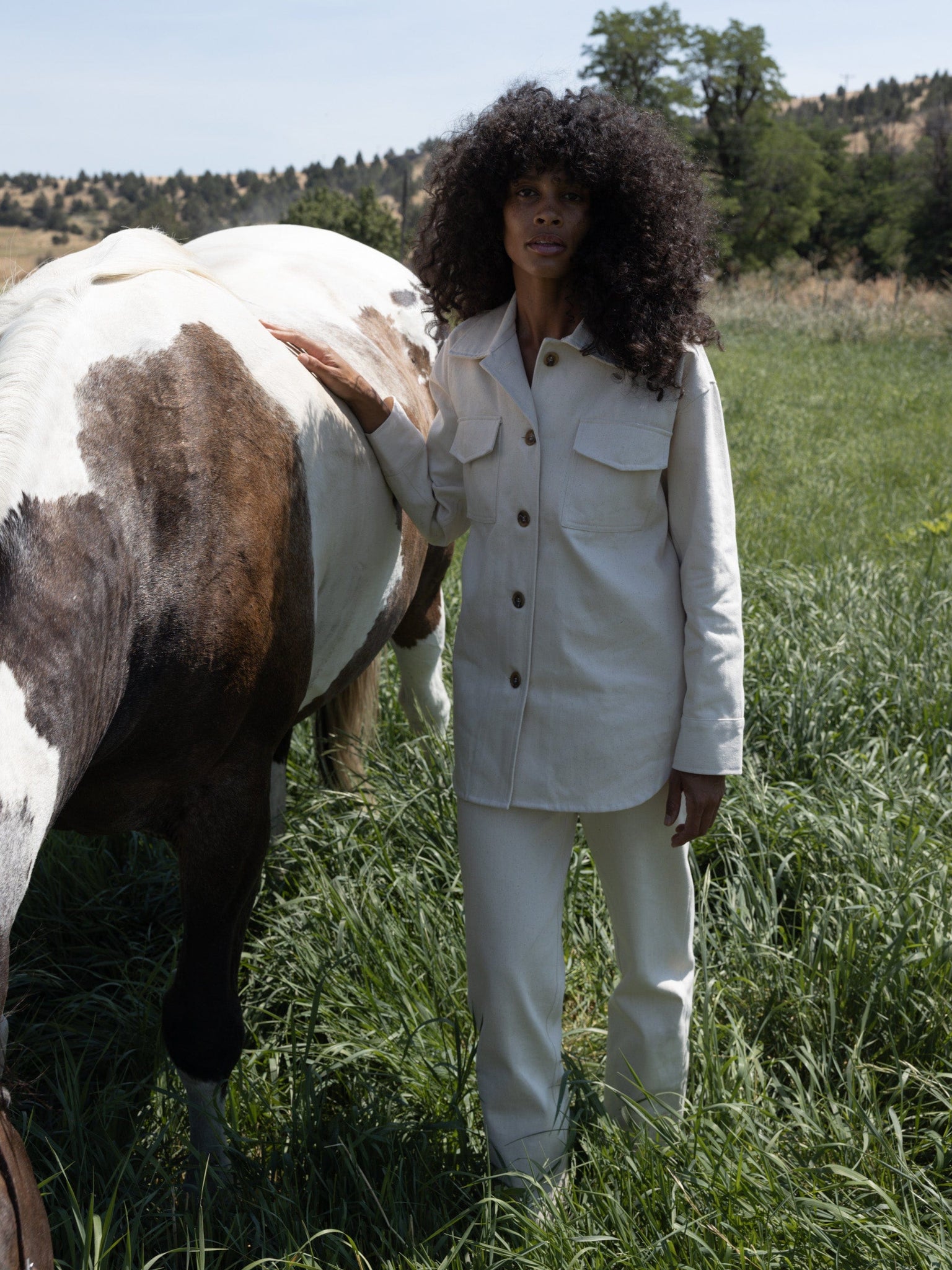 A woman wearing a Roan Shirt Jacket - Bone is standing next to a horse.