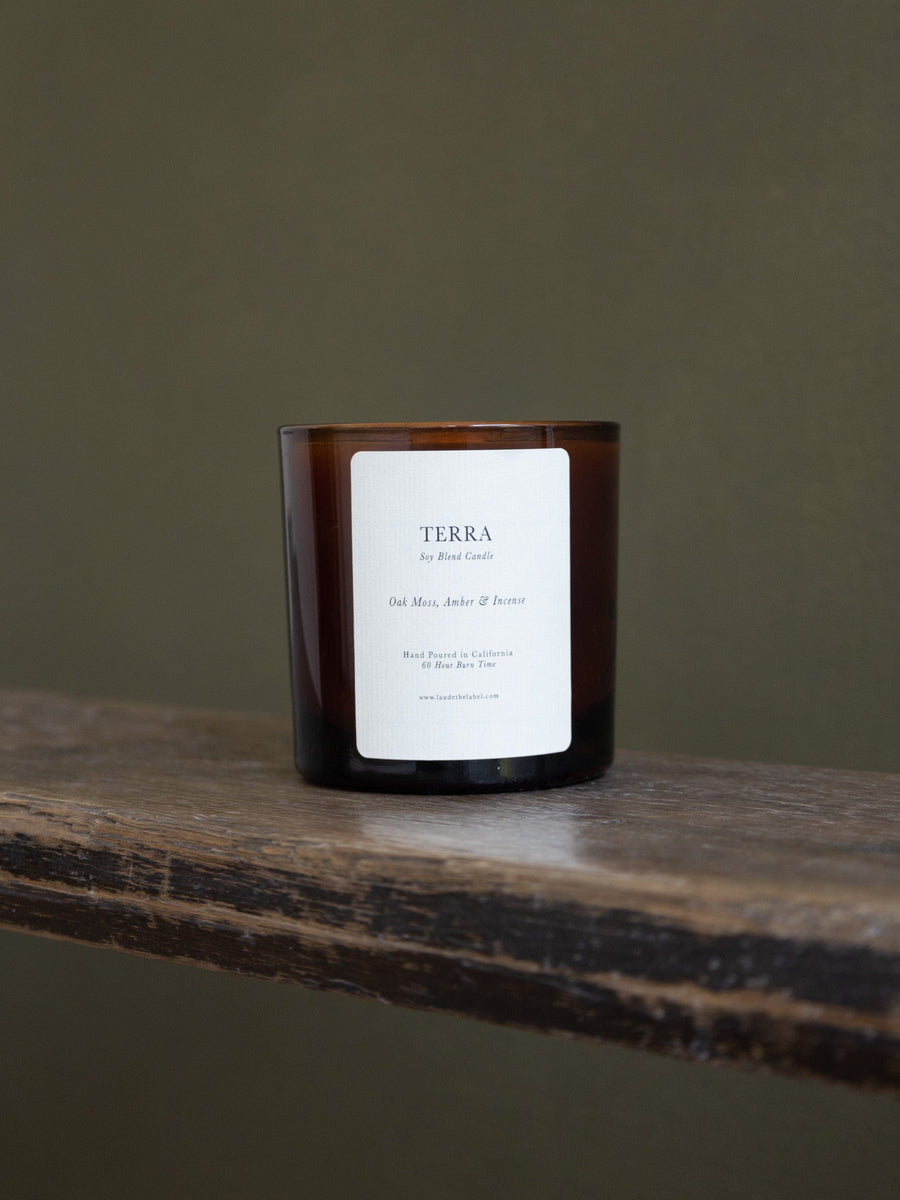 A Terra Glass Candle made with a coconut & soy wax blend, sitting on top of a wooden table.