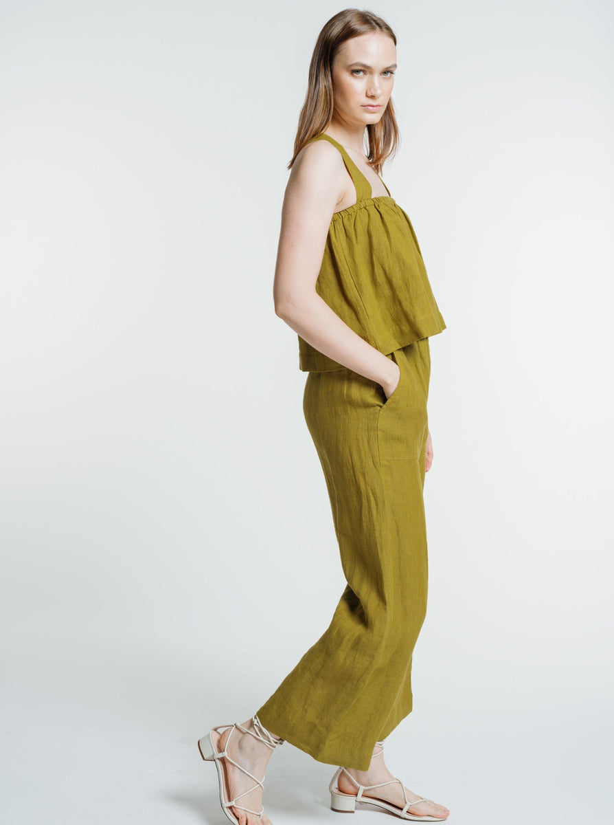 The model is wearing a mustard jumpsuit and Everyday Crop - Dried Tobacco sandals.