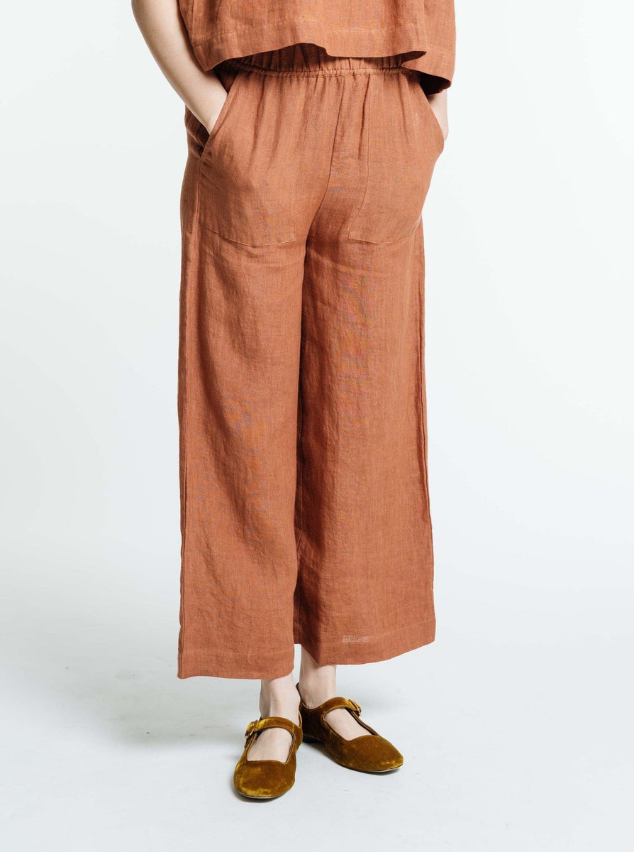 A woman is standing in an Everyday Crop - Amber Brown linen jumpsuit.