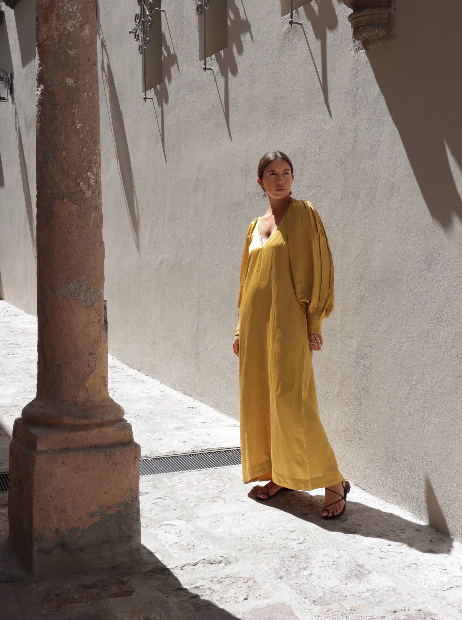 A woman in a Lupita Maxi Dress - Citrine standing next to pillars.