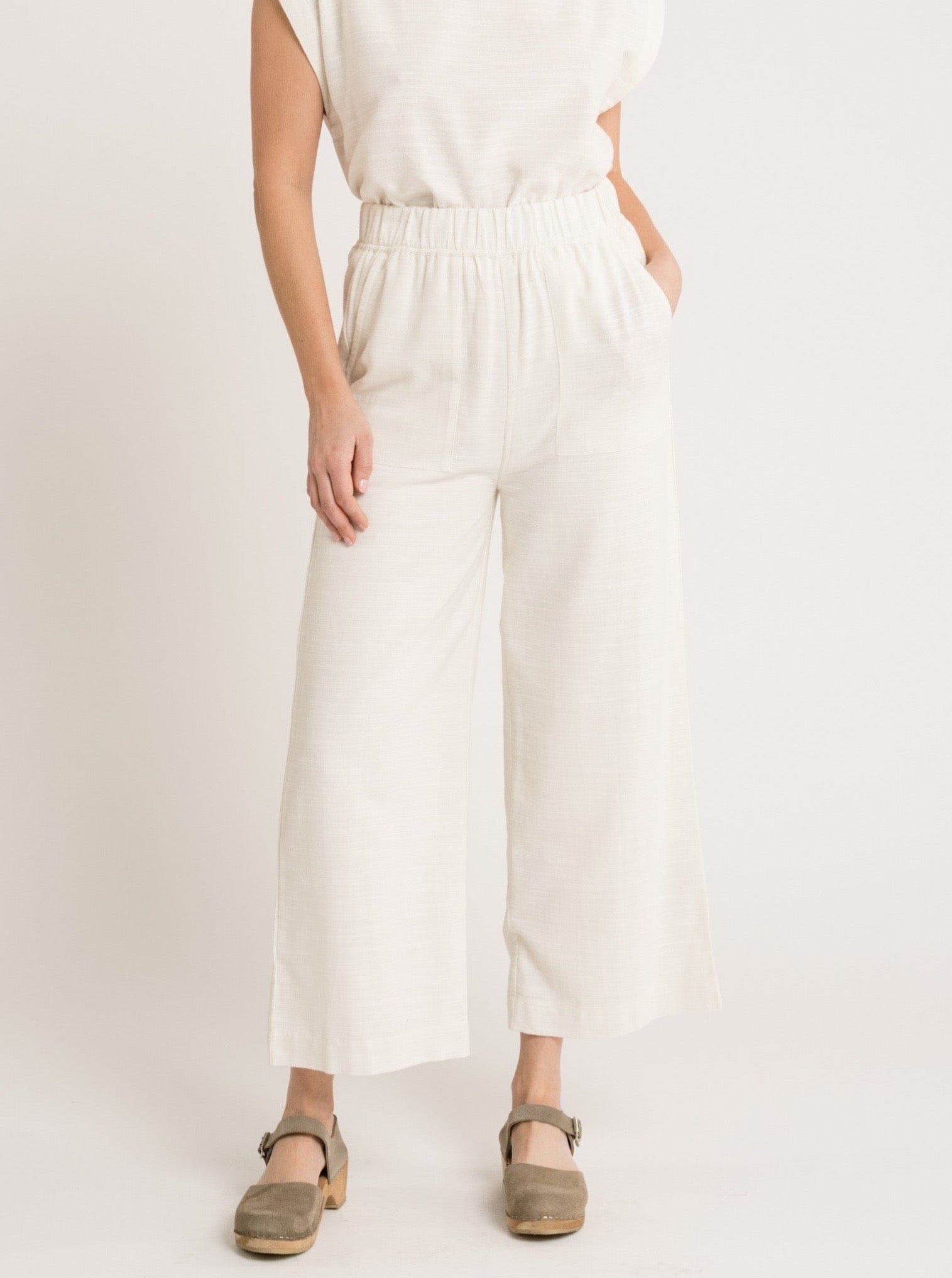 A woman wearing the Everyday Crop Pant - Ivory jumpsuit and sandals.