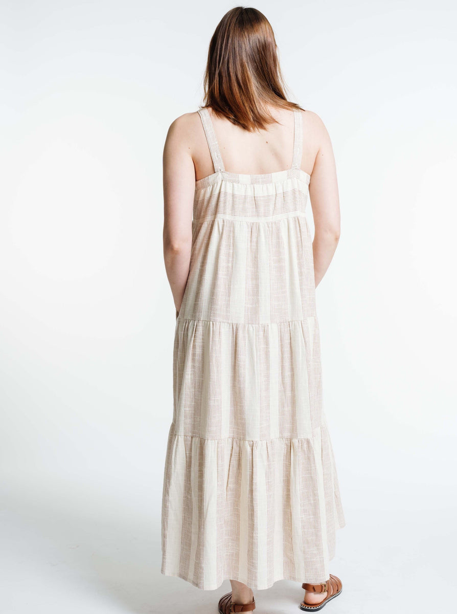 The back view of a woman wearing a Strappy Tiered Maxi Dress - Terracotta Ticking Stripe with adjustable straps.