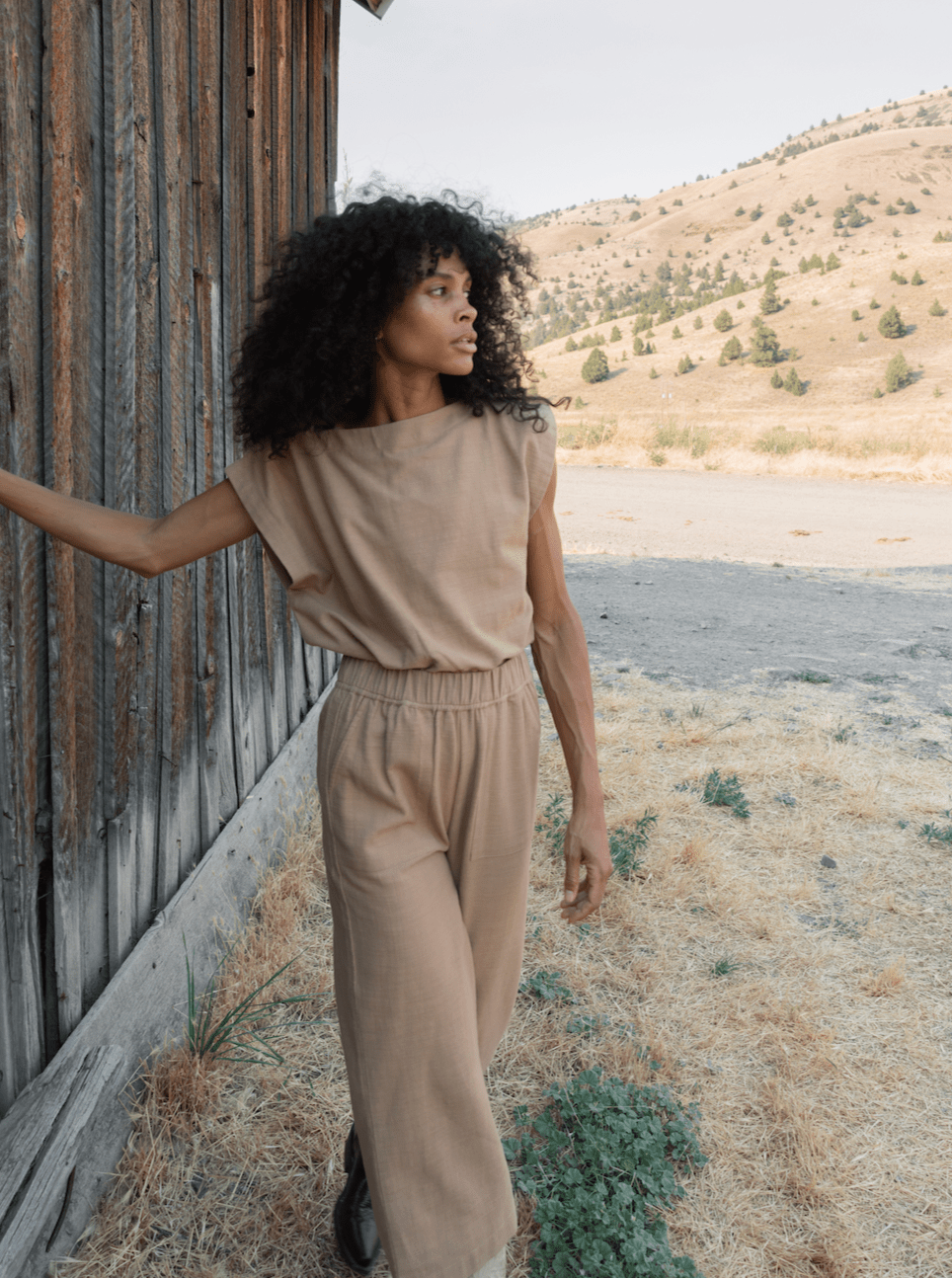 A black woman in the Everyday Top - Tannin certified organic cotton jumpsuit standing in front of a barn.