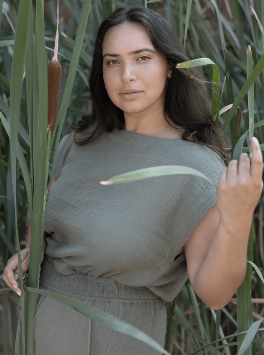 A woman in an Everyday Top - Sagebrush standing next to tall reeds made of organic cotton.