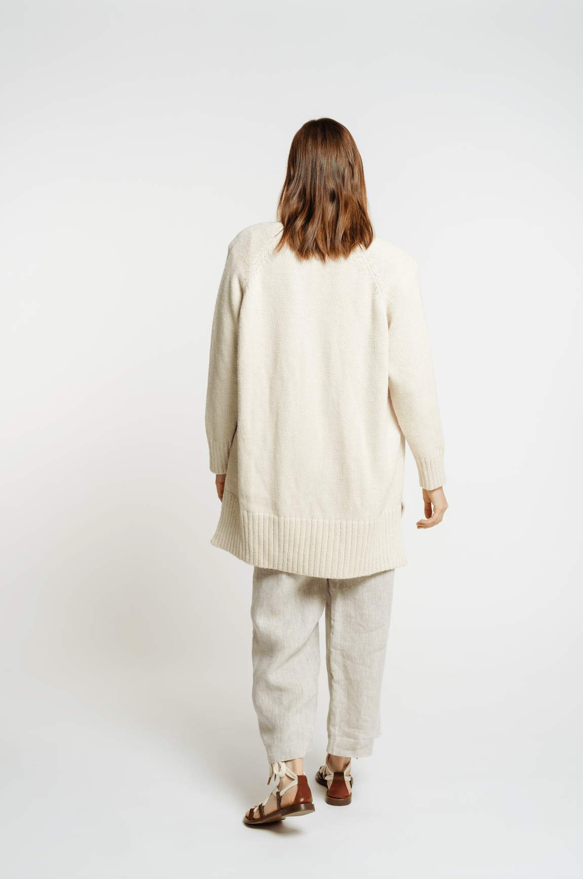 The back of a woman wearing a Valley Cardigan - Vanilla sweater and pants.