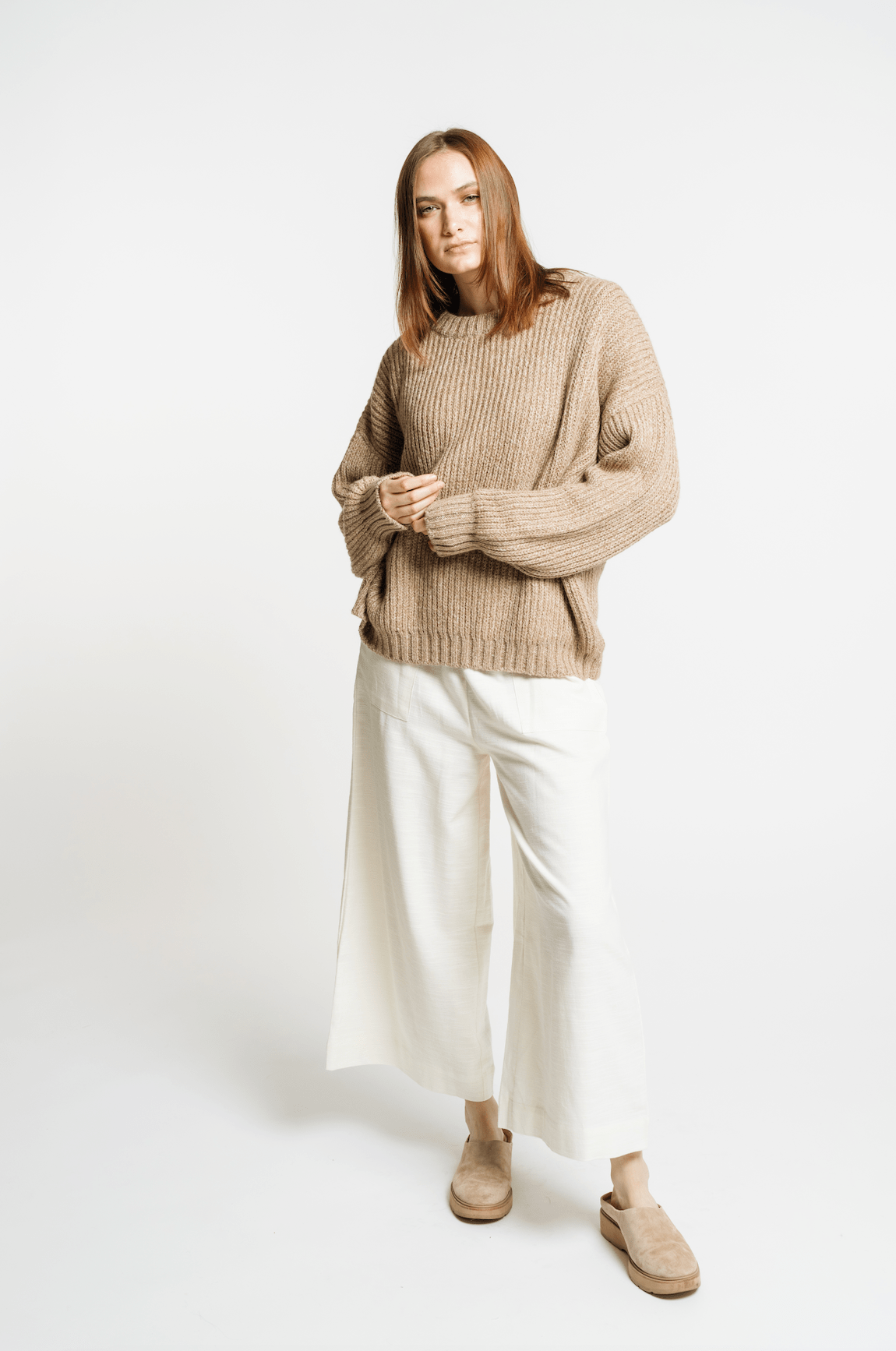 The model is wearing a Field Sweater - Caramel and white wide leg pants.