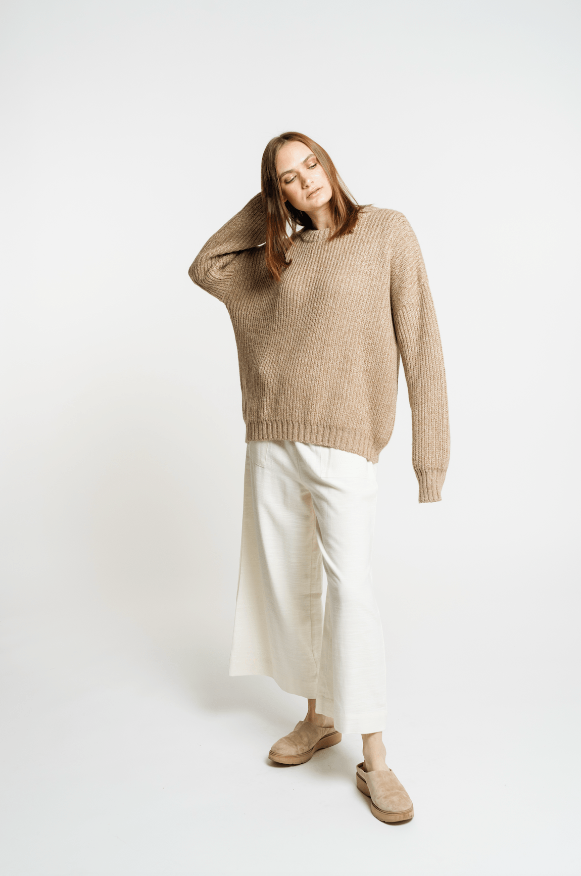 The model is wearing a Field Sweater - Caramel and white pants.