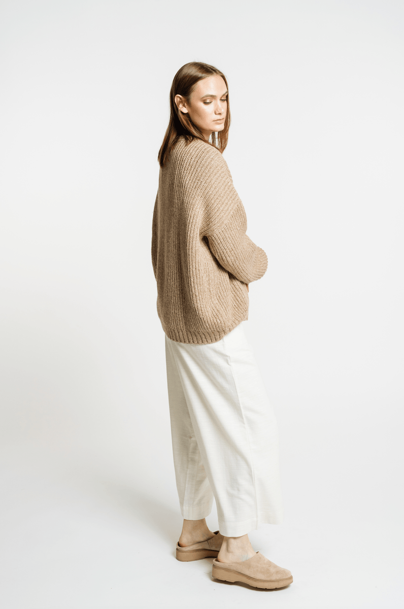 The model is wearing a Field Sweater - Caramel and white pants.
