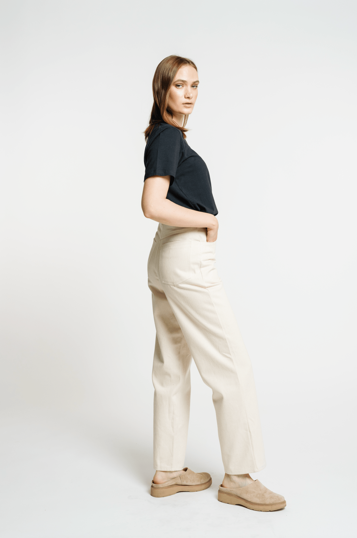 The model is wearing a black t-shirt and beige pants, accessorized with handcrafted details on the Camp Pant - Bone - Sample.