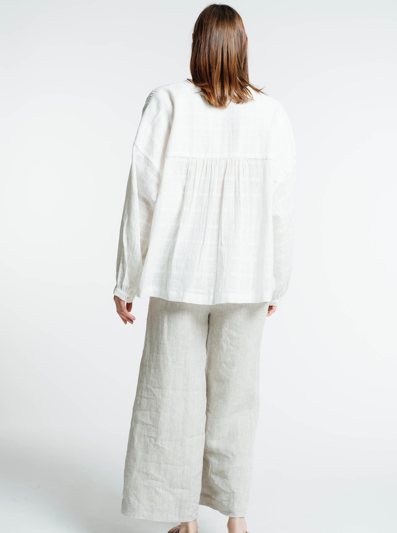 The back view of a woman wearing the Francoise Top - Alabaster Plaid blouse and wide leg pants.