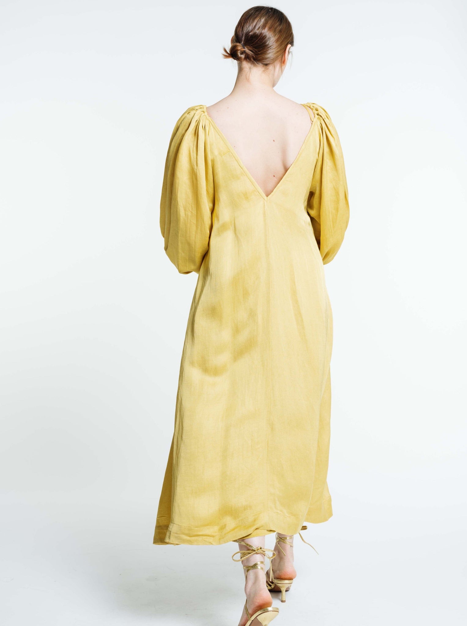 The back view of a woman wearing a Lupita Maxi Dress - Citrine made of satin fabric.